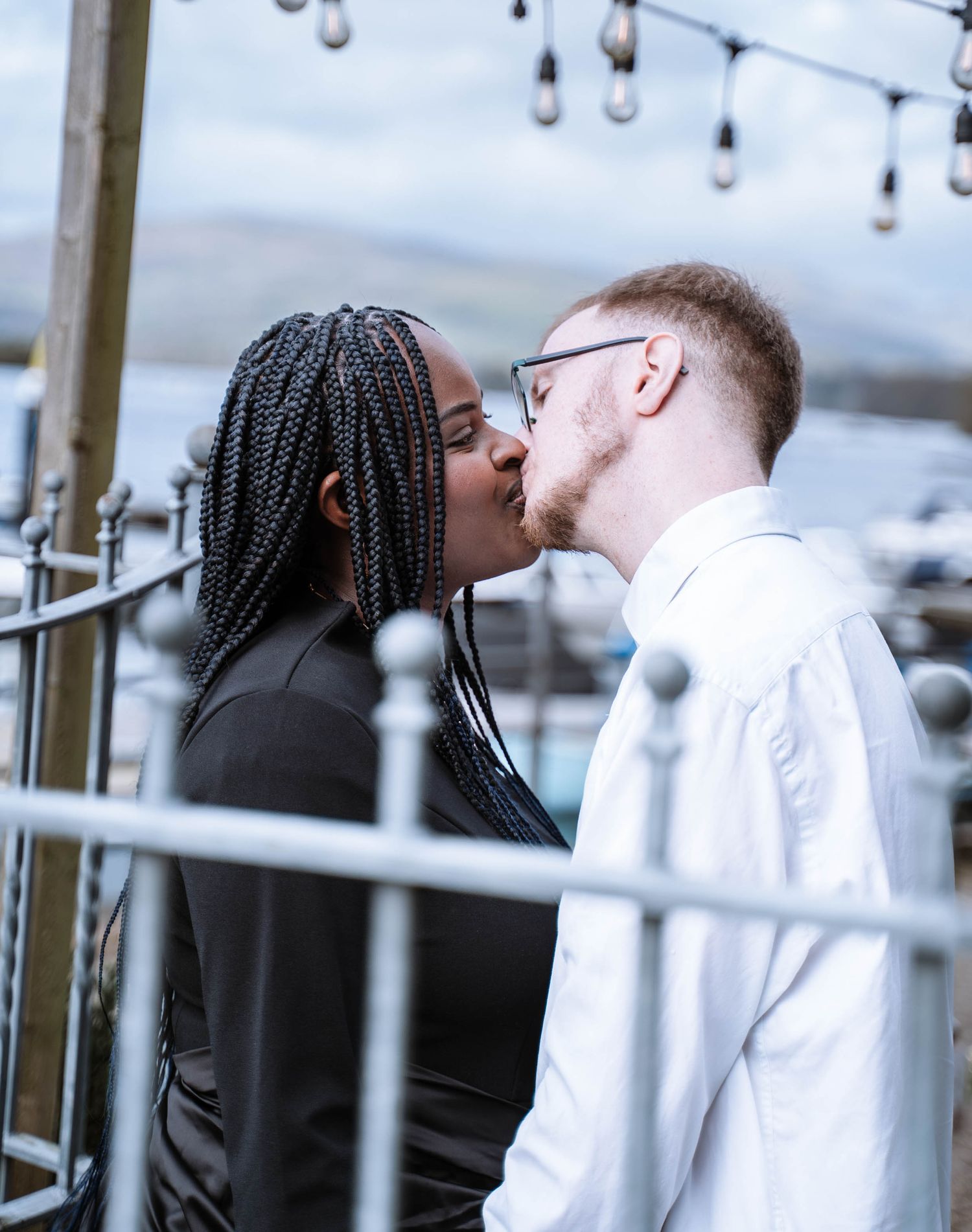 Interracial couple kissing beside the lakeside railings in Windermere, Lake District