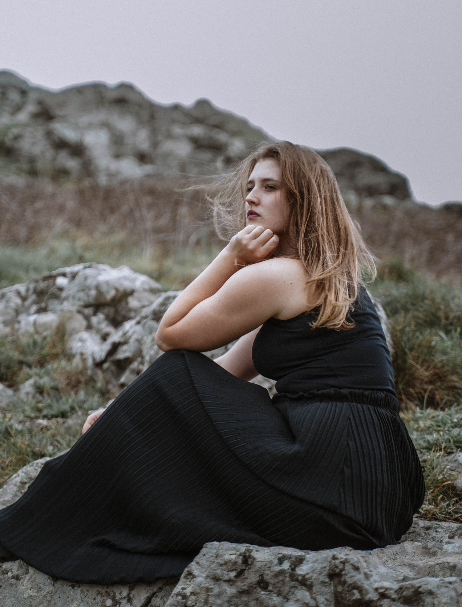 Gothic Cornwall elopement portrait of a person in a black dress lying on rocky terrain in St Ives under overcast skies