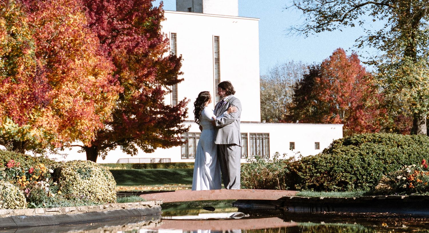 Couple embracing near LDS temple with autumn trees during wedding portraits