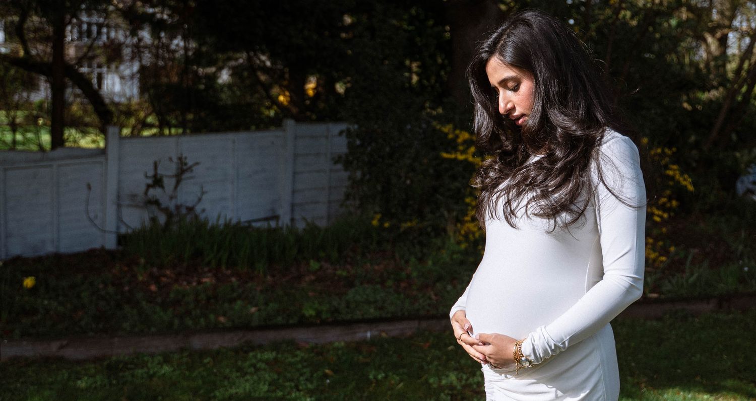 Pregnant woman standing in her garden with both hands resting on her baby bump