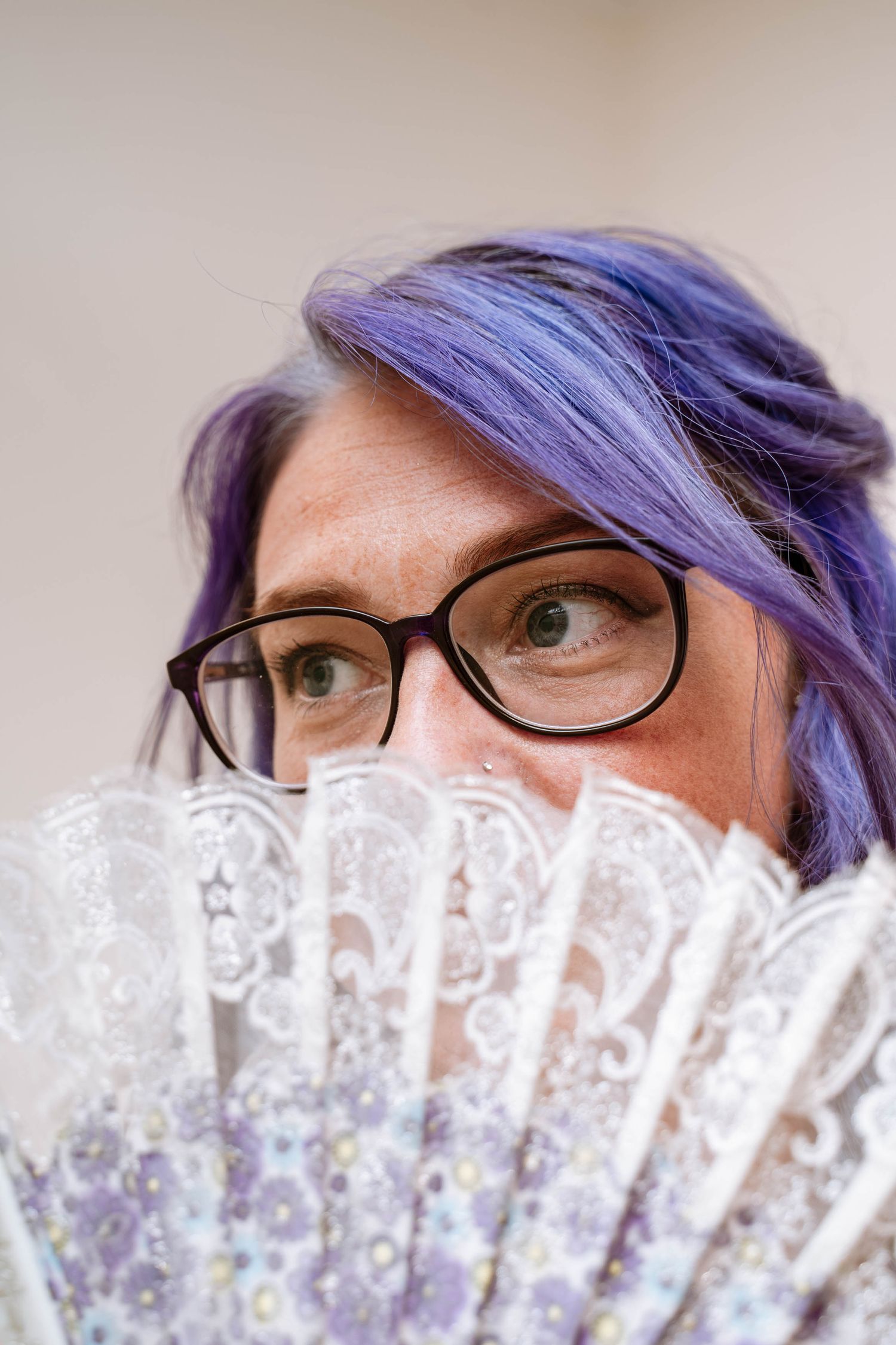 Bride with purple hair smiling behind a lace fan at their registry wedding at The Lodge, Mesnes Park