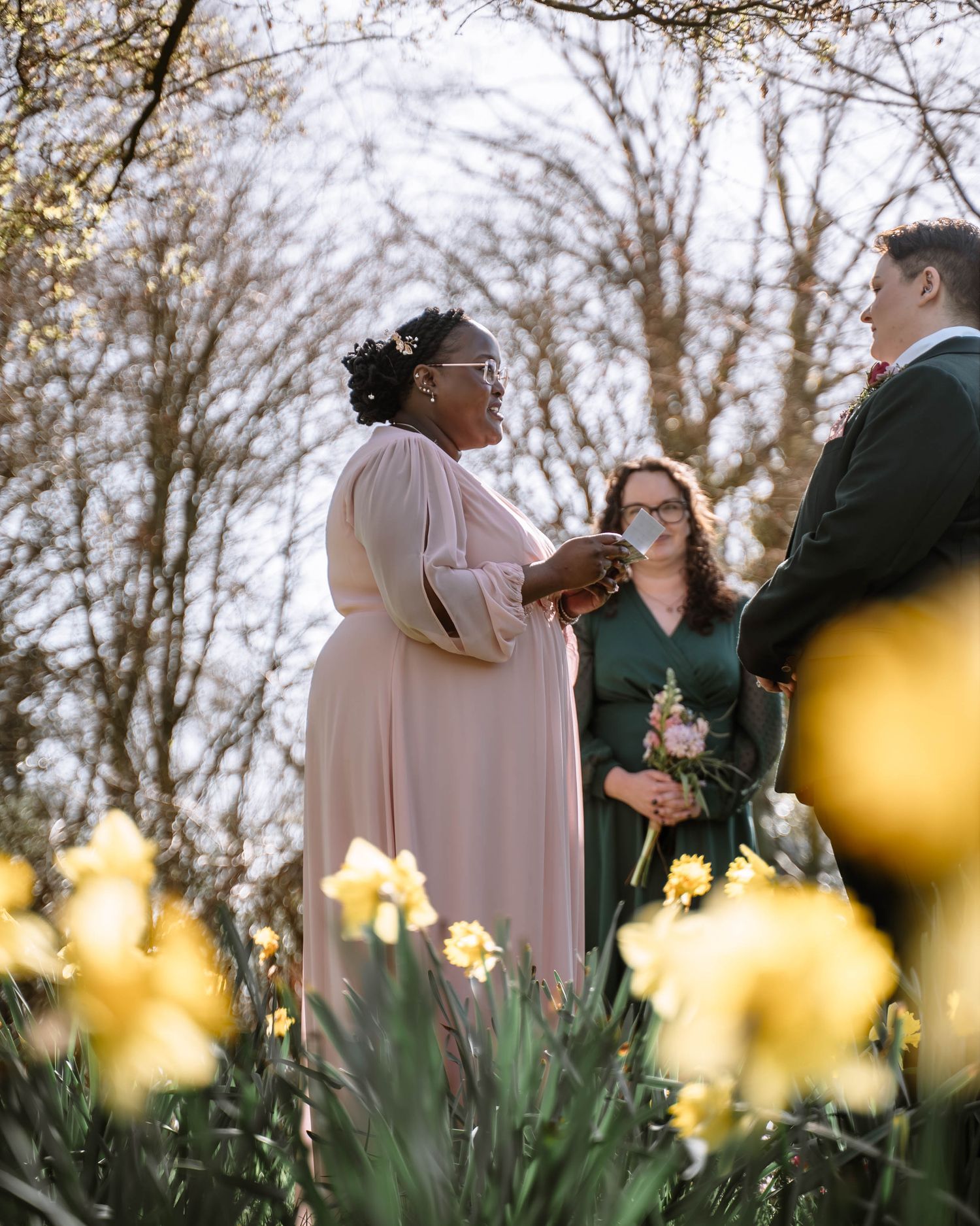 Couple exchanging vows outdoors among flowers during Manchester LGBTQ wedding ceremony