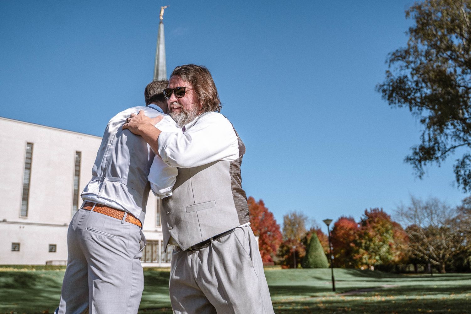 Groom and Best Man hugging outdoors near LDS temple during wedding portraits