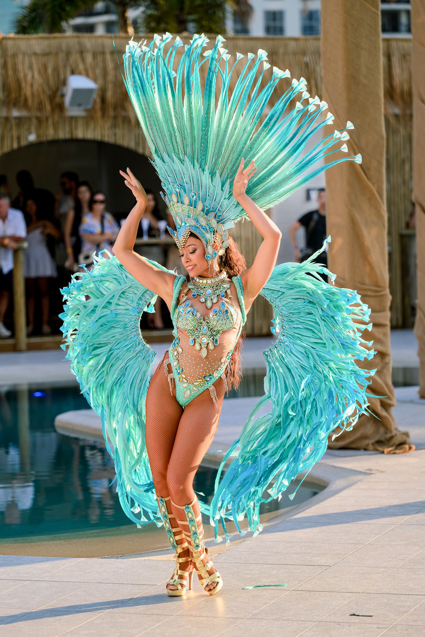 Performer in turquoise feathered carnival costume dancing by poolside.
