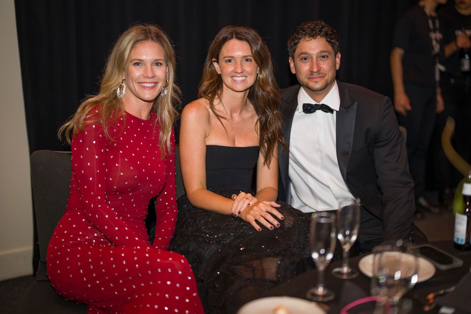 Three guests in formal attire seated at an elegant dinner table during an upscale event.