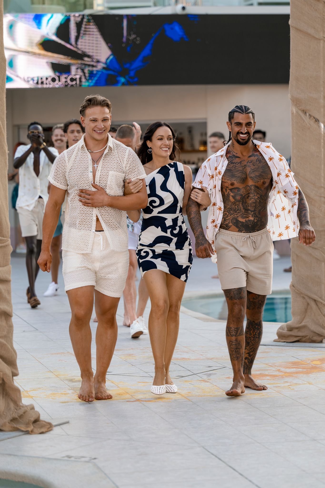 Models walking runway in casual summer resort wear at poolside fashion show.