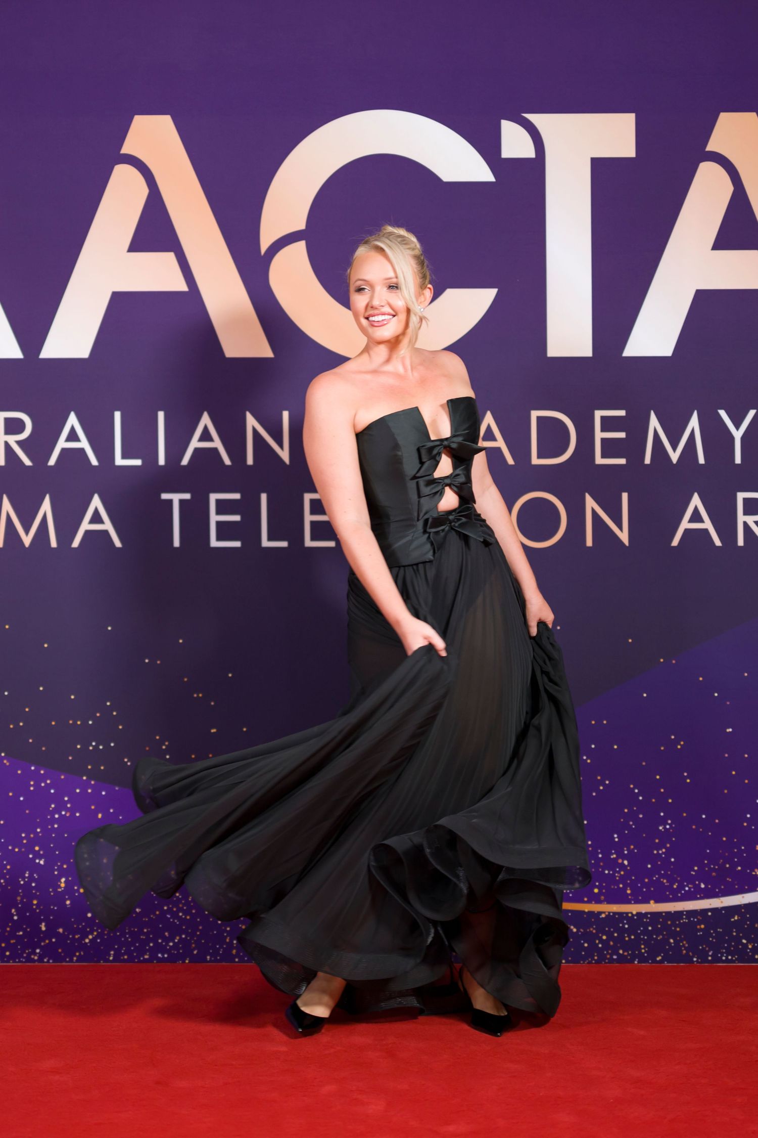 Elegant black evening gown flowing on red carpet at AACTA Awards with purple backdrop.