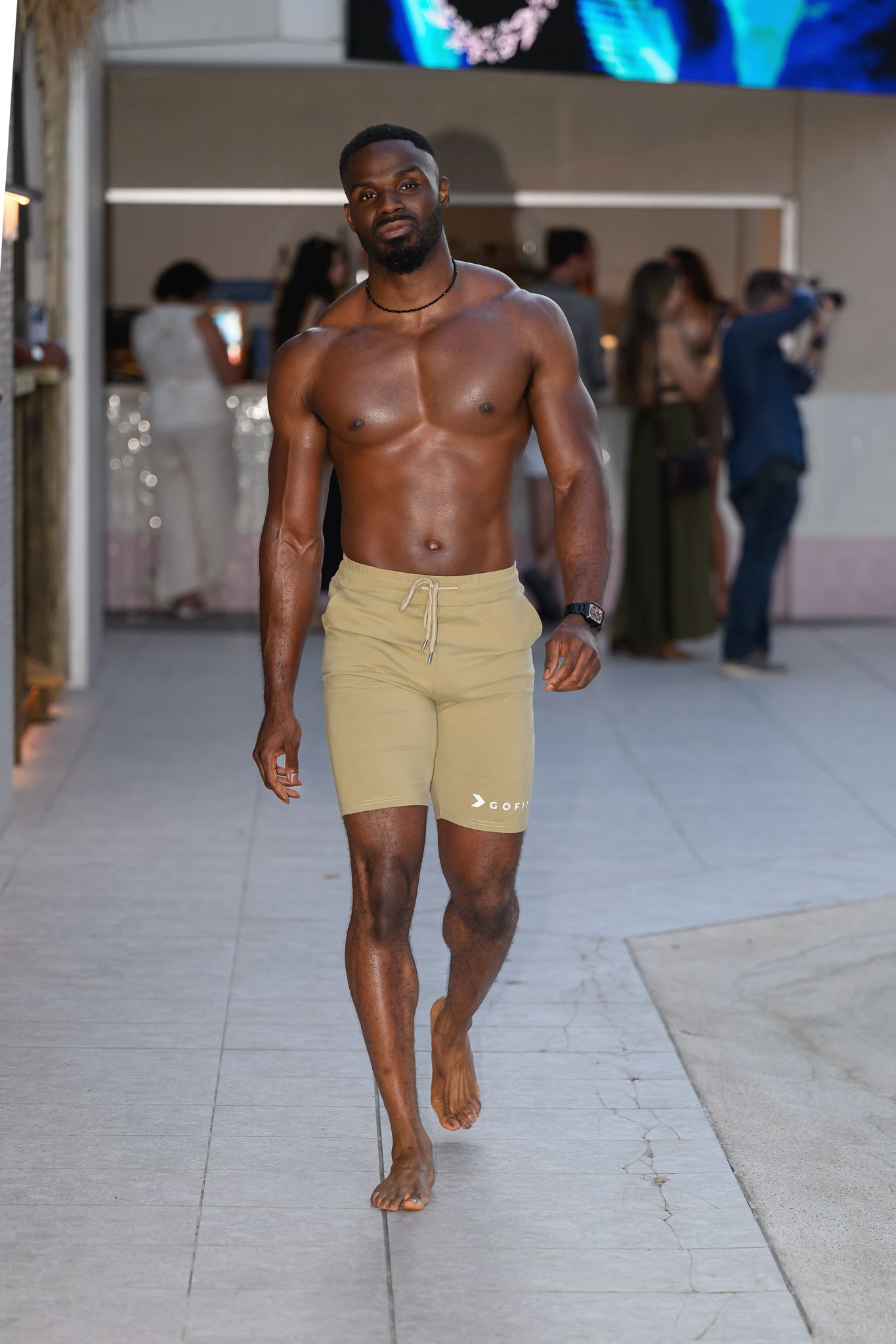 Athletic models showcase beige shorts collection on indoor runway.