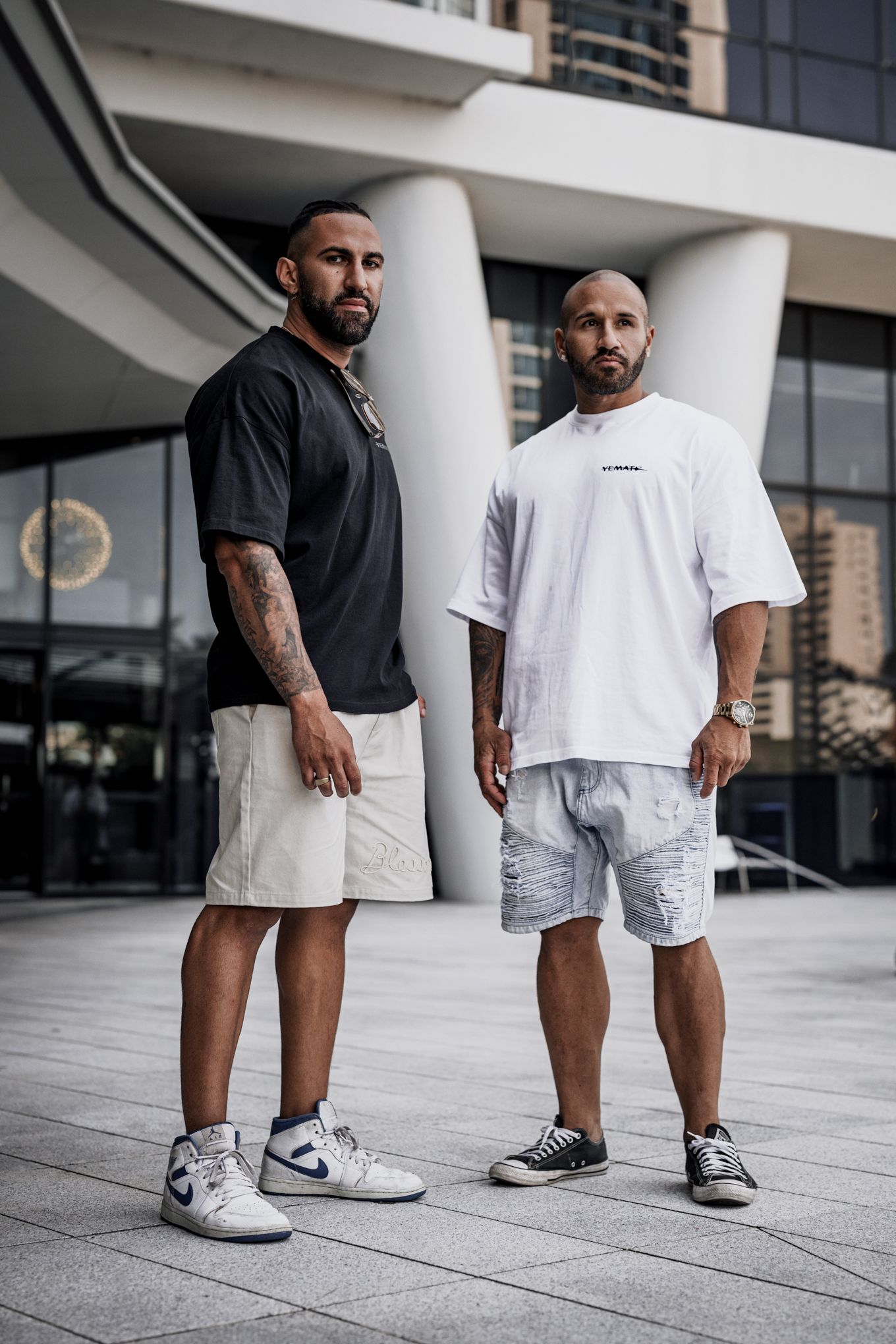 Two people in casual white and black outfits with sneakers standing on modern plaza.