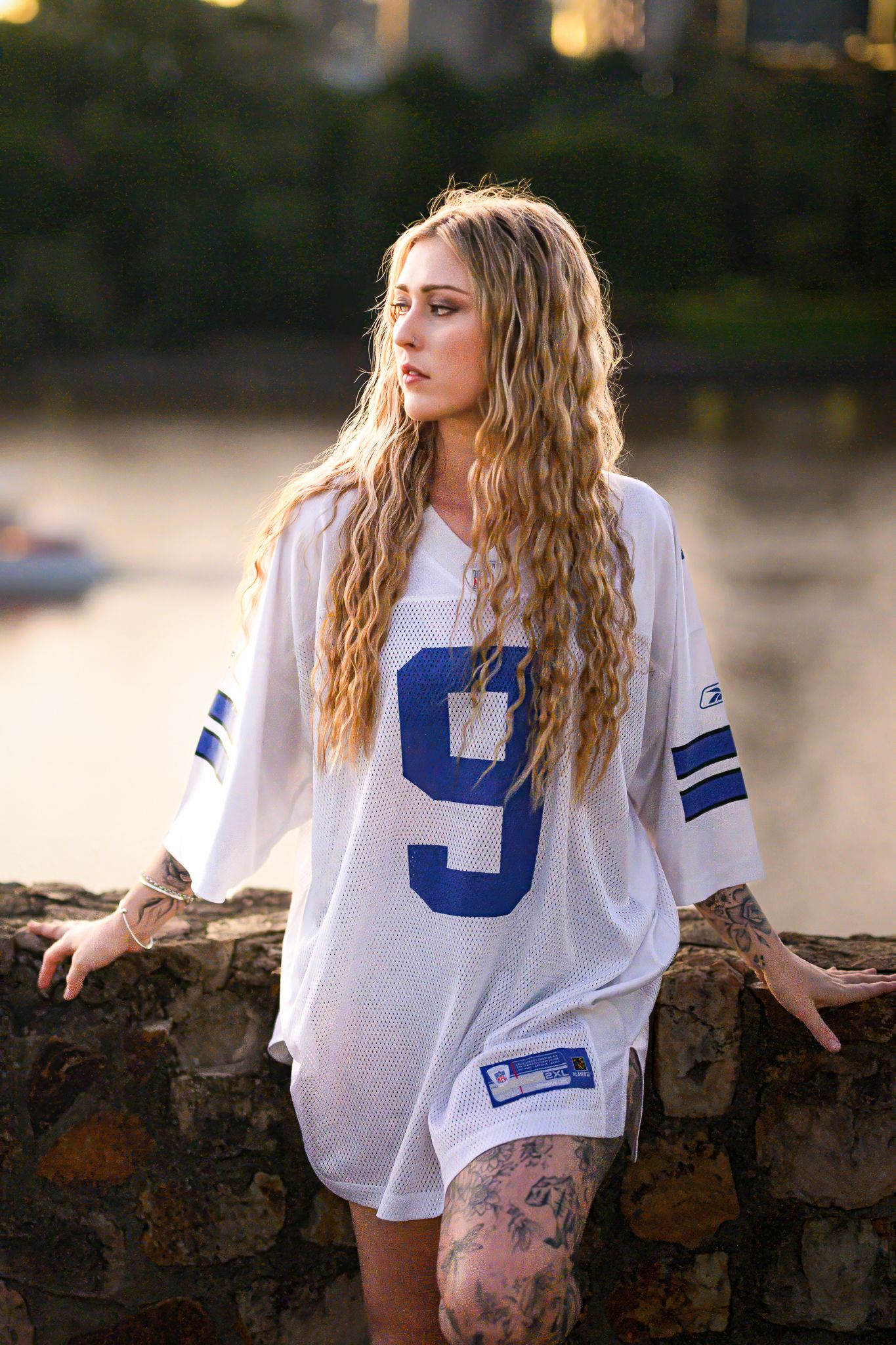 Athletic figure in oversized white jersey poses casually against stone wall.