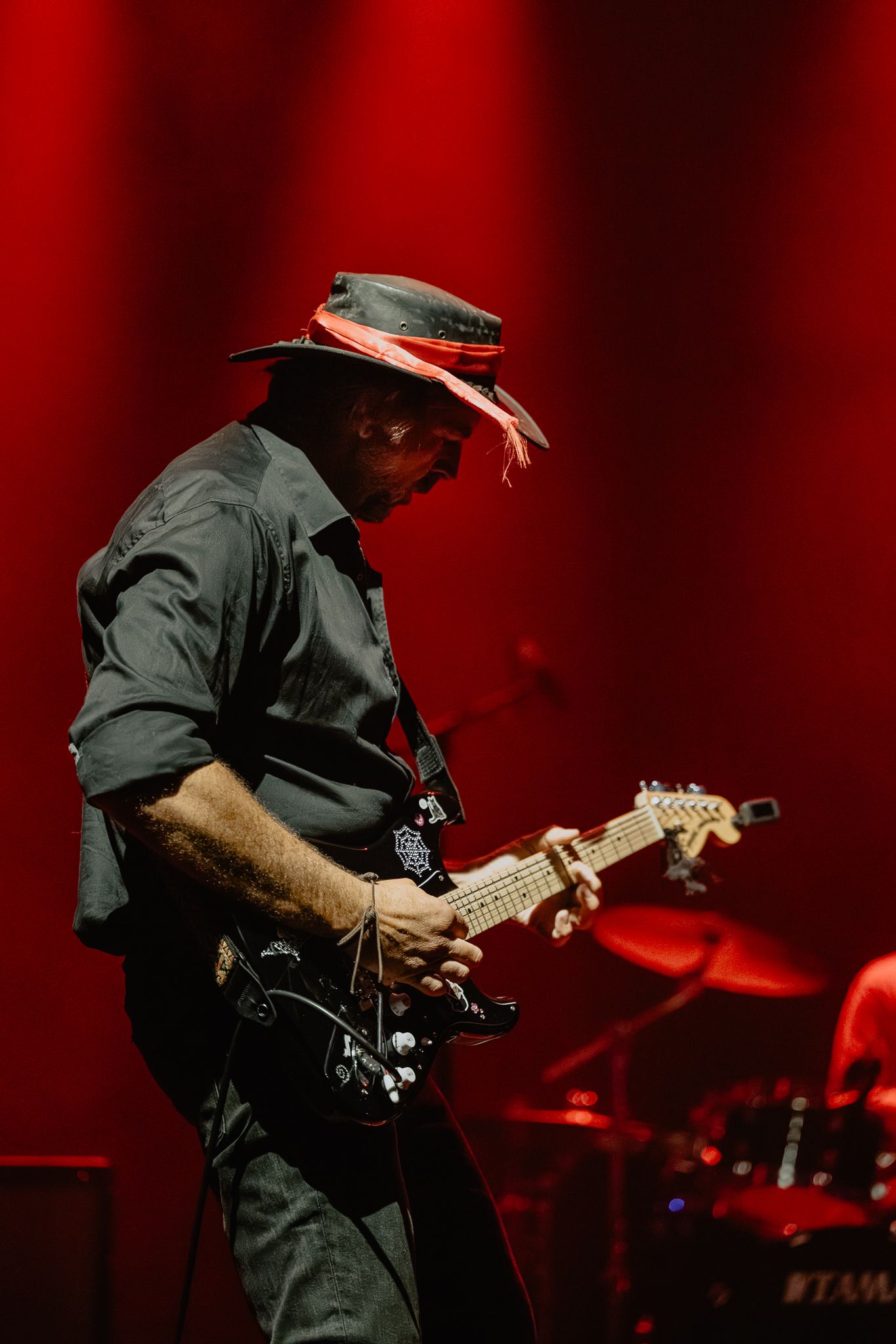 Guitarist performing on stage bathed in dramatic red lighting during a live concert performance.