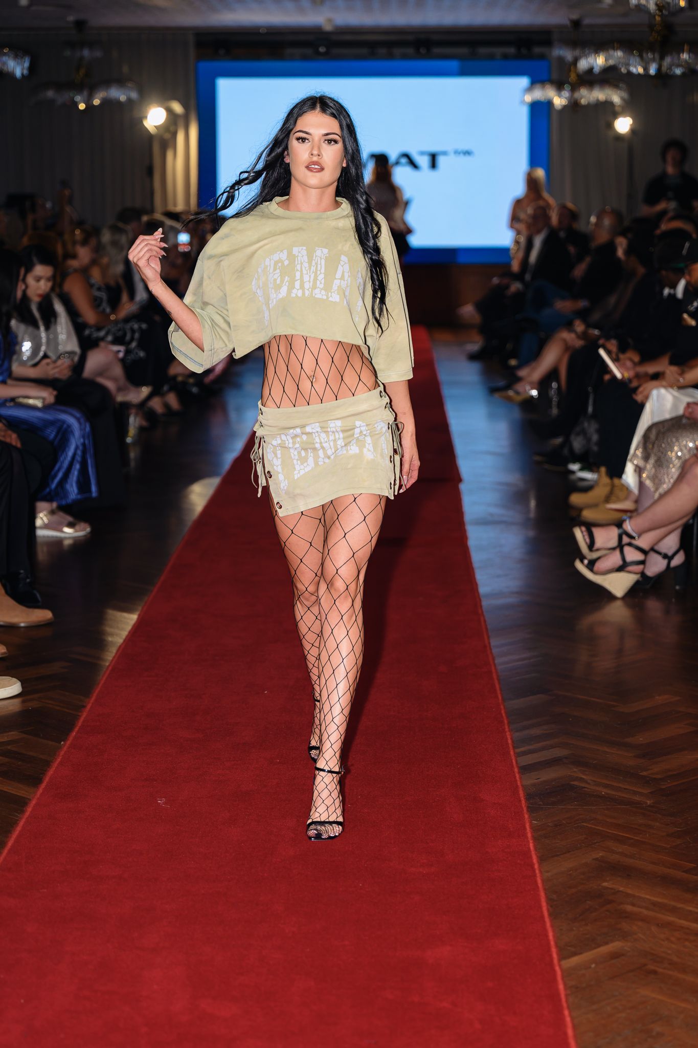 Model wearing cream sweater and fishnet stockings struts down red carpet runway.