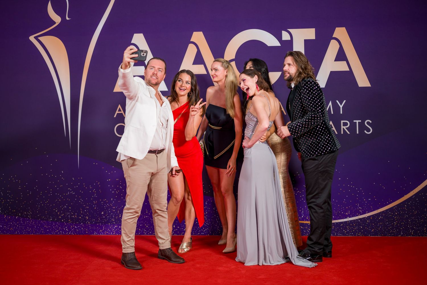 Group taking selfie together at AACTA Awards on red carpet with purple backdrop.