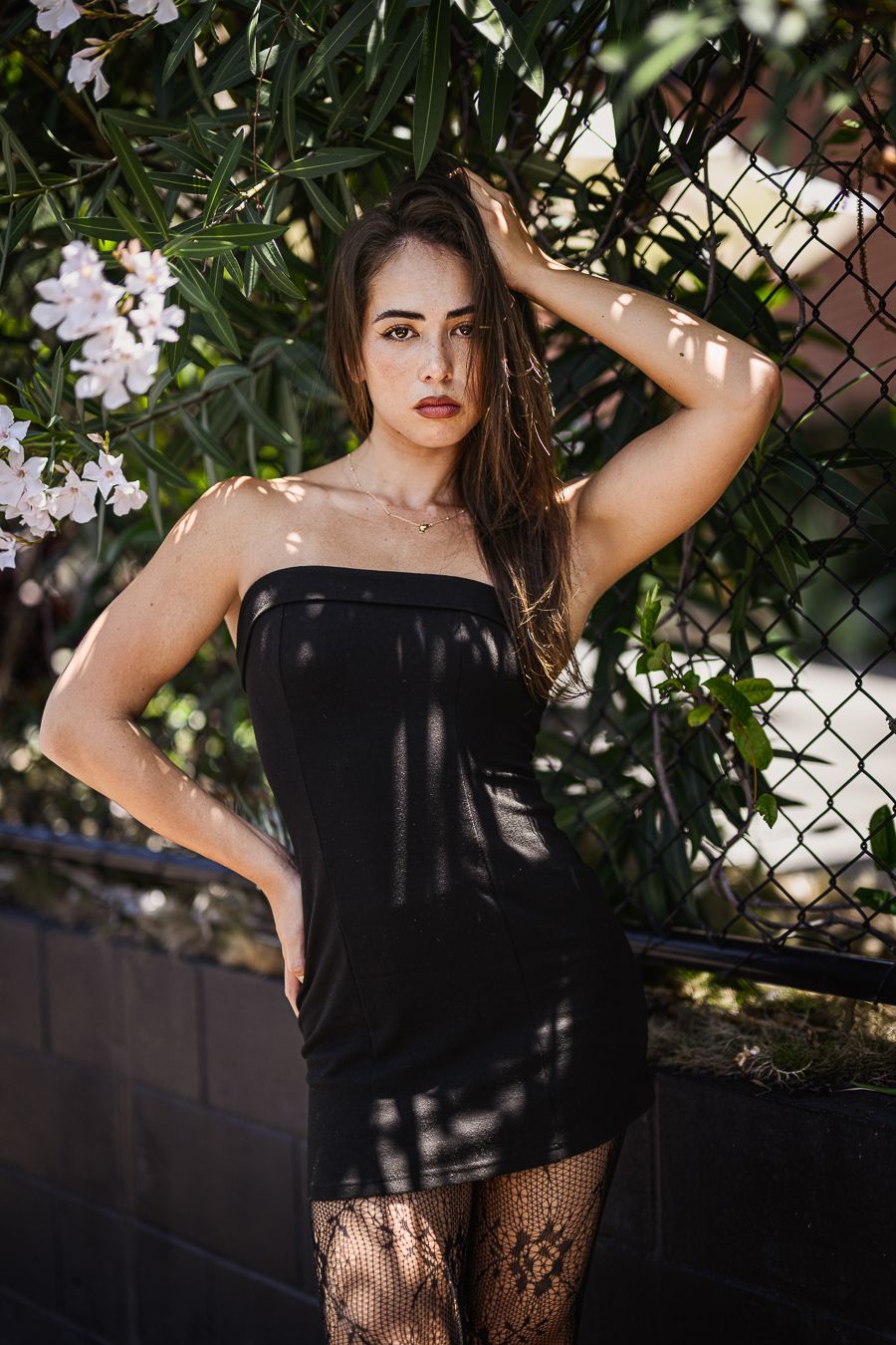 Person in black top poses against foliage and chain link fence backdrop.