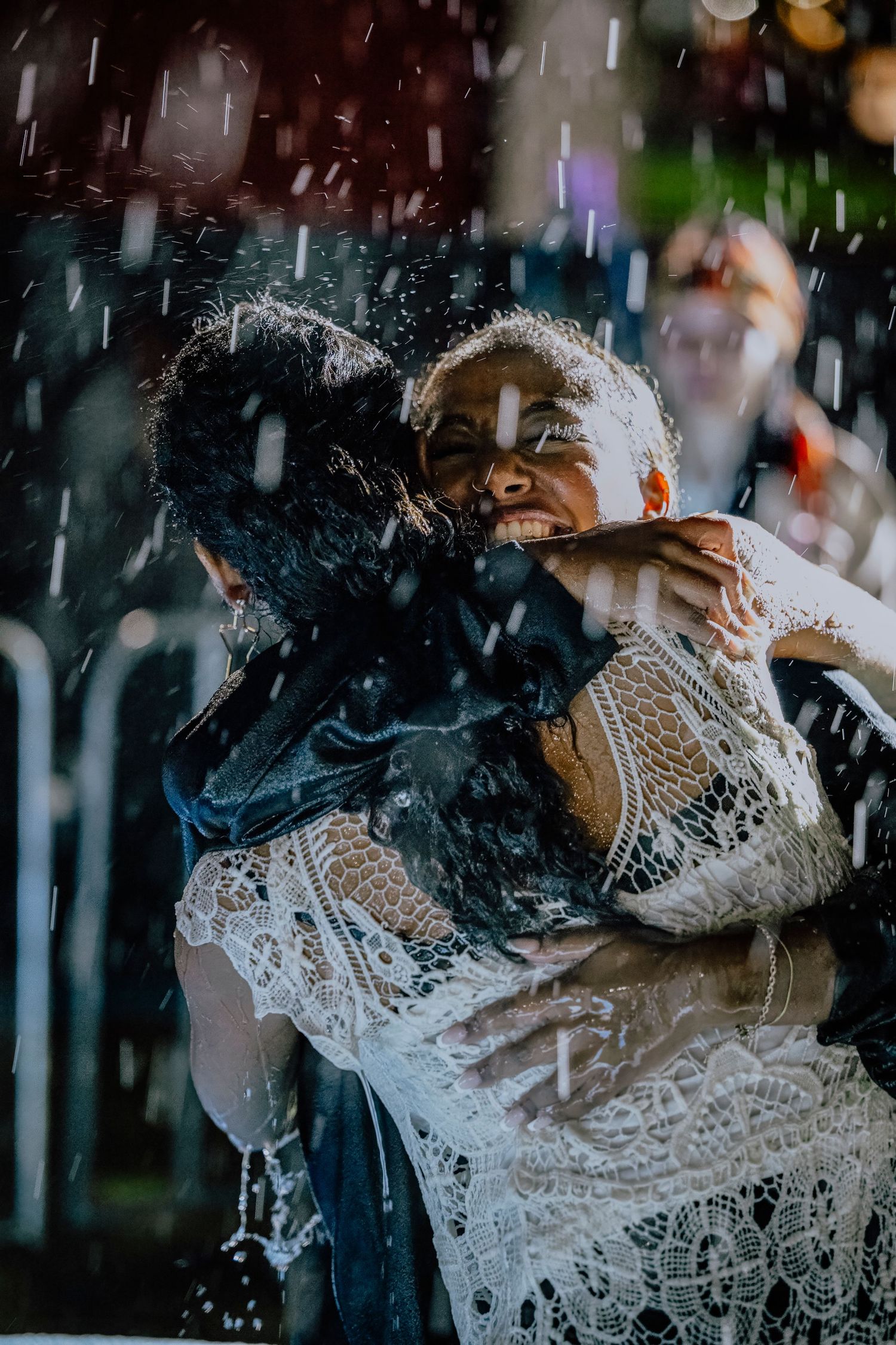 Two people embracing in the rain, one wearing a white lace dress, captured in a dramatic, emotional outdoor moment.