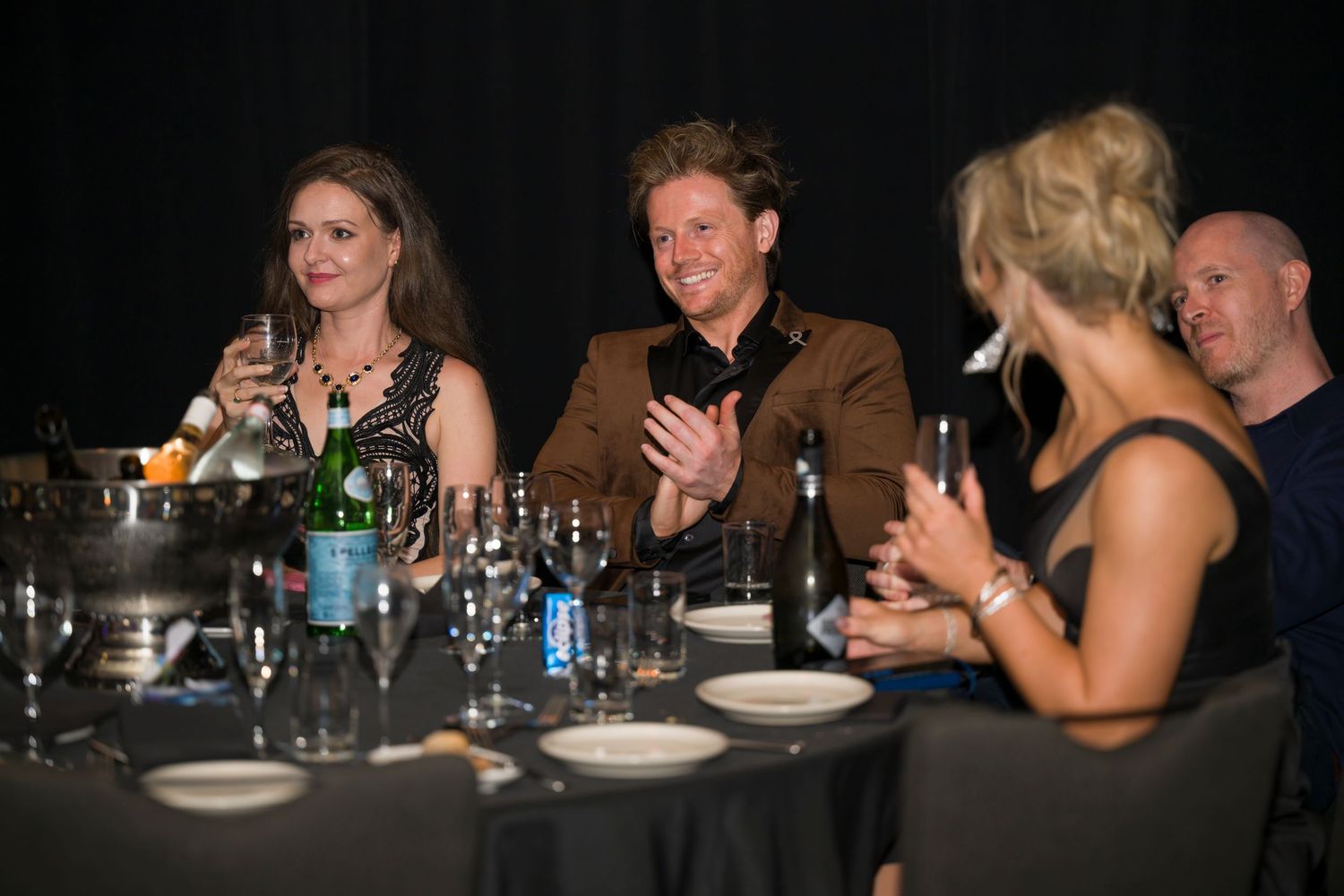 Event attendees applauding while seated at a formal dinner table.