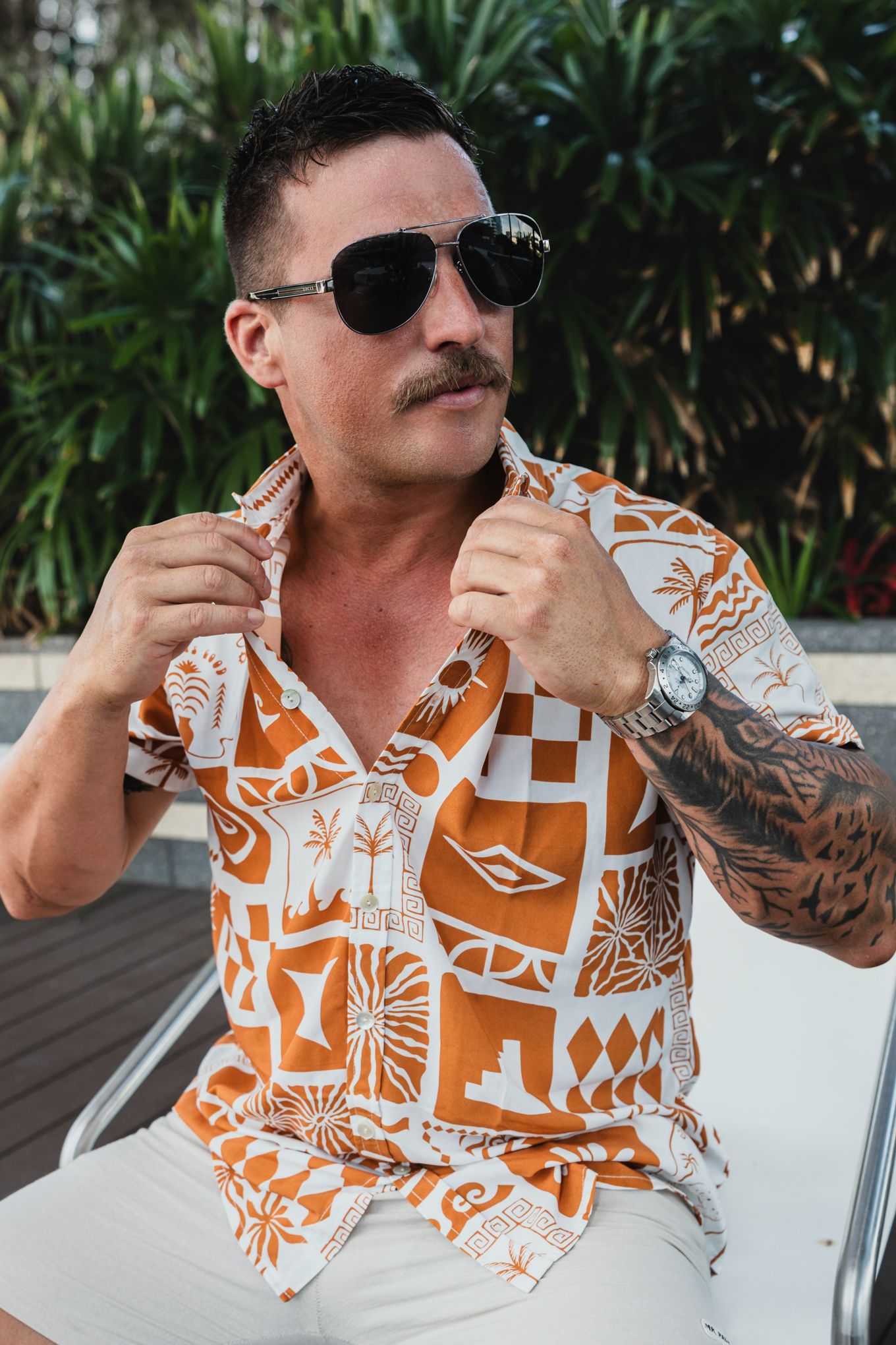Person in orange and white patterned shirt relaxing in tropical setting.