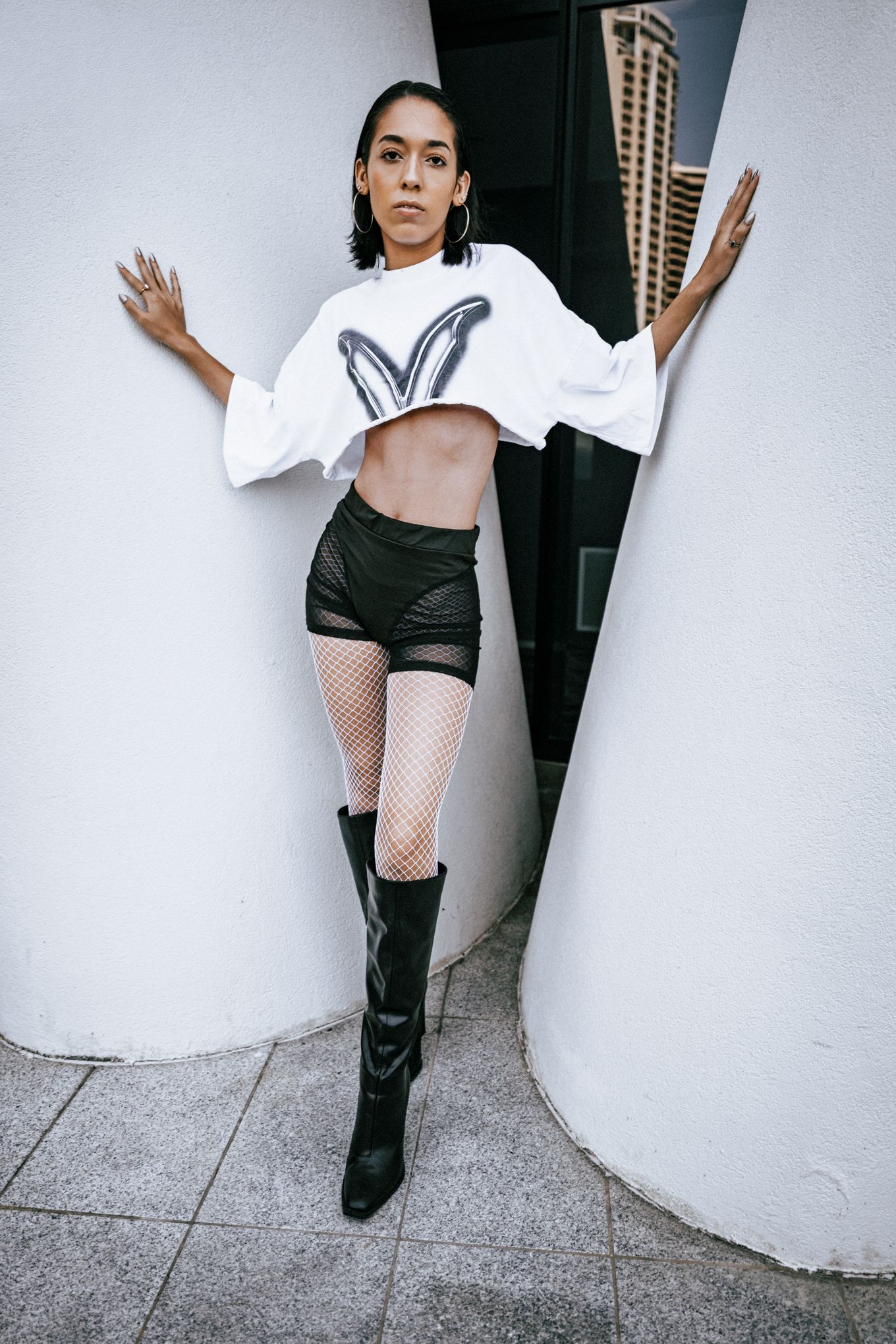 Fashion series showing black boots and fishnet stockings against white wall.