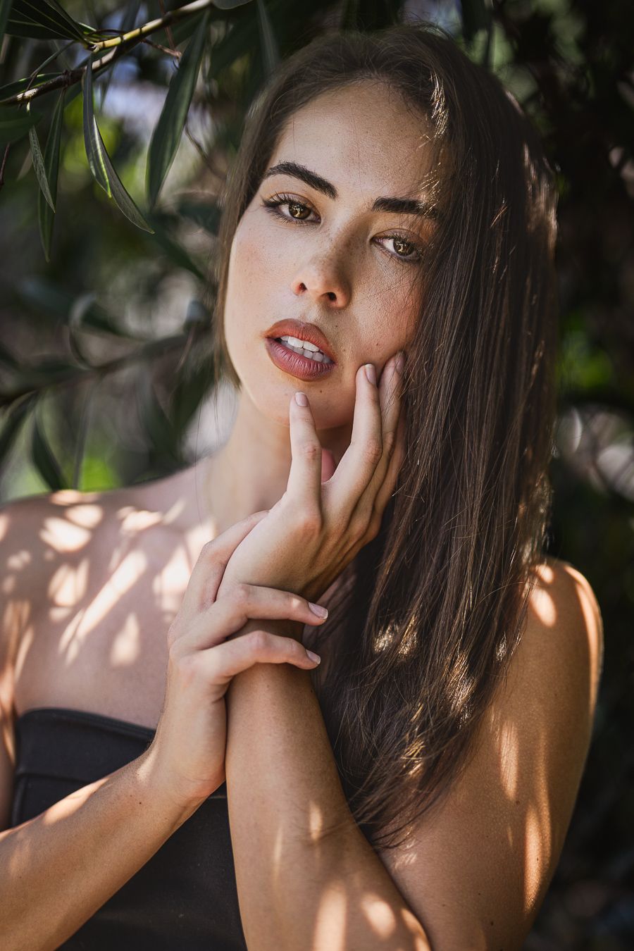 Portrait with dappled sunlight through leaves creating dramatic shadows.