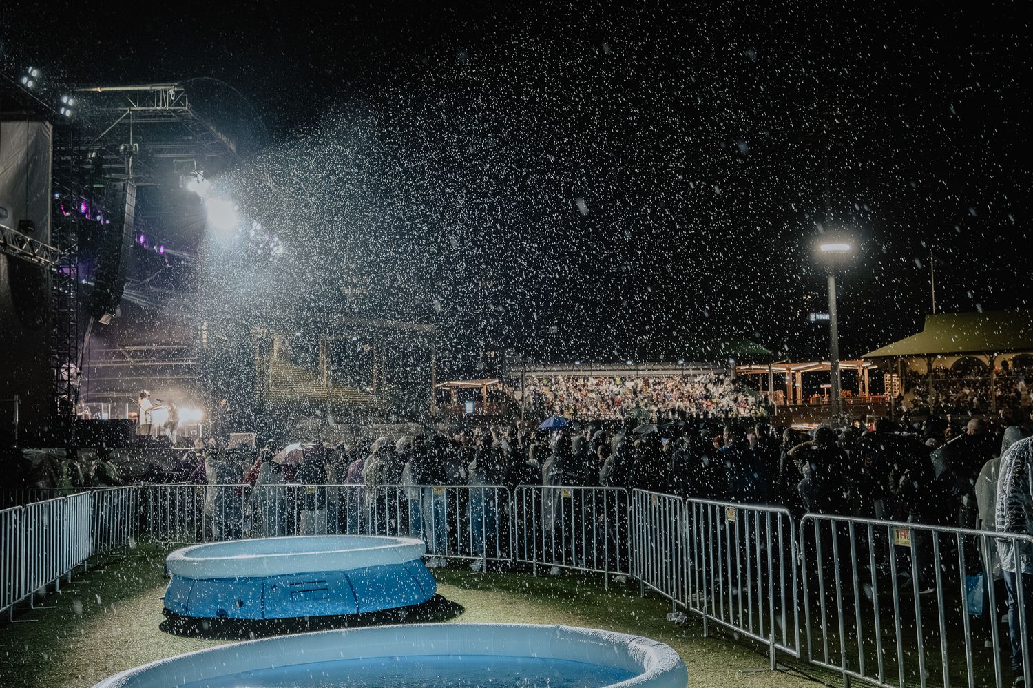Outdoor nighttime event with illuminated barriers and crowd under starry sky.