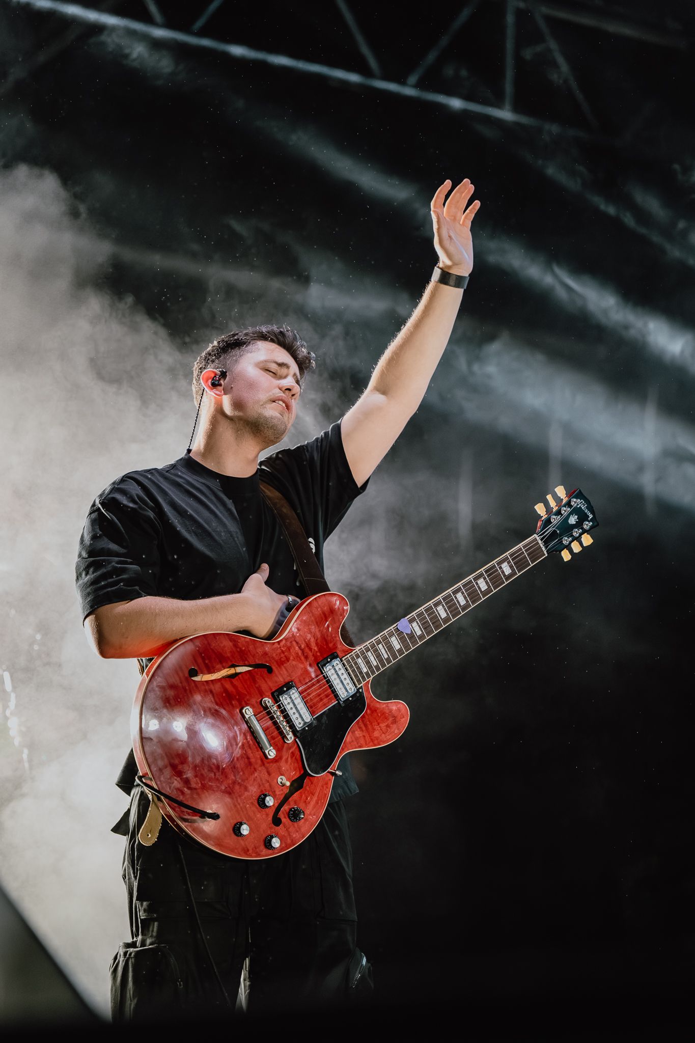 Performer playing red electric guitar on stage with atmospheric smoke effects.
