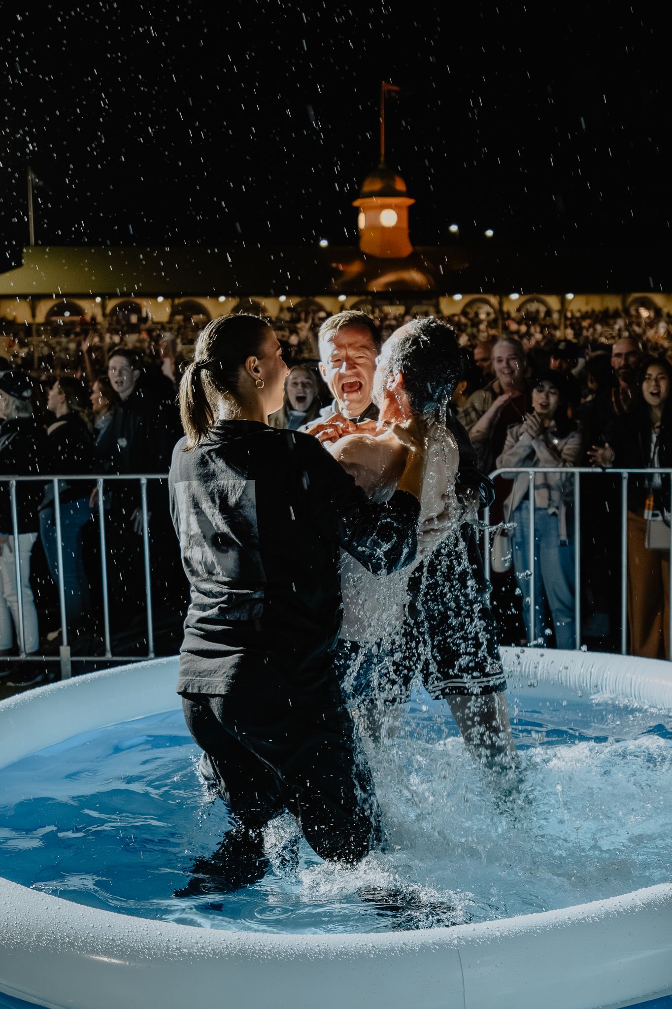 People participating in a baptism ceremony in an outdoor pool at night.