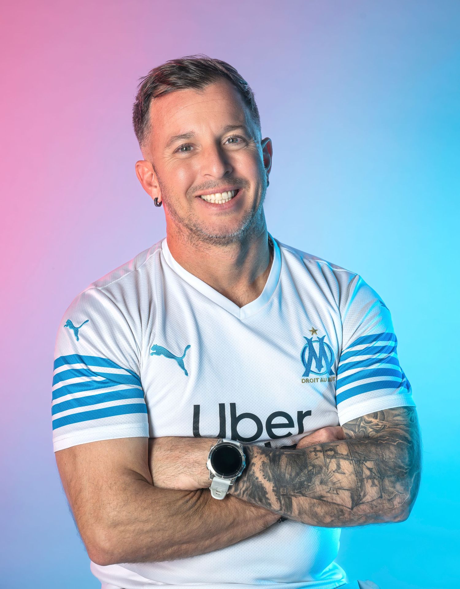 Professional athlete poses in white Olympique Marseille jersey with Uber sponsor against pink and blue gradient background.