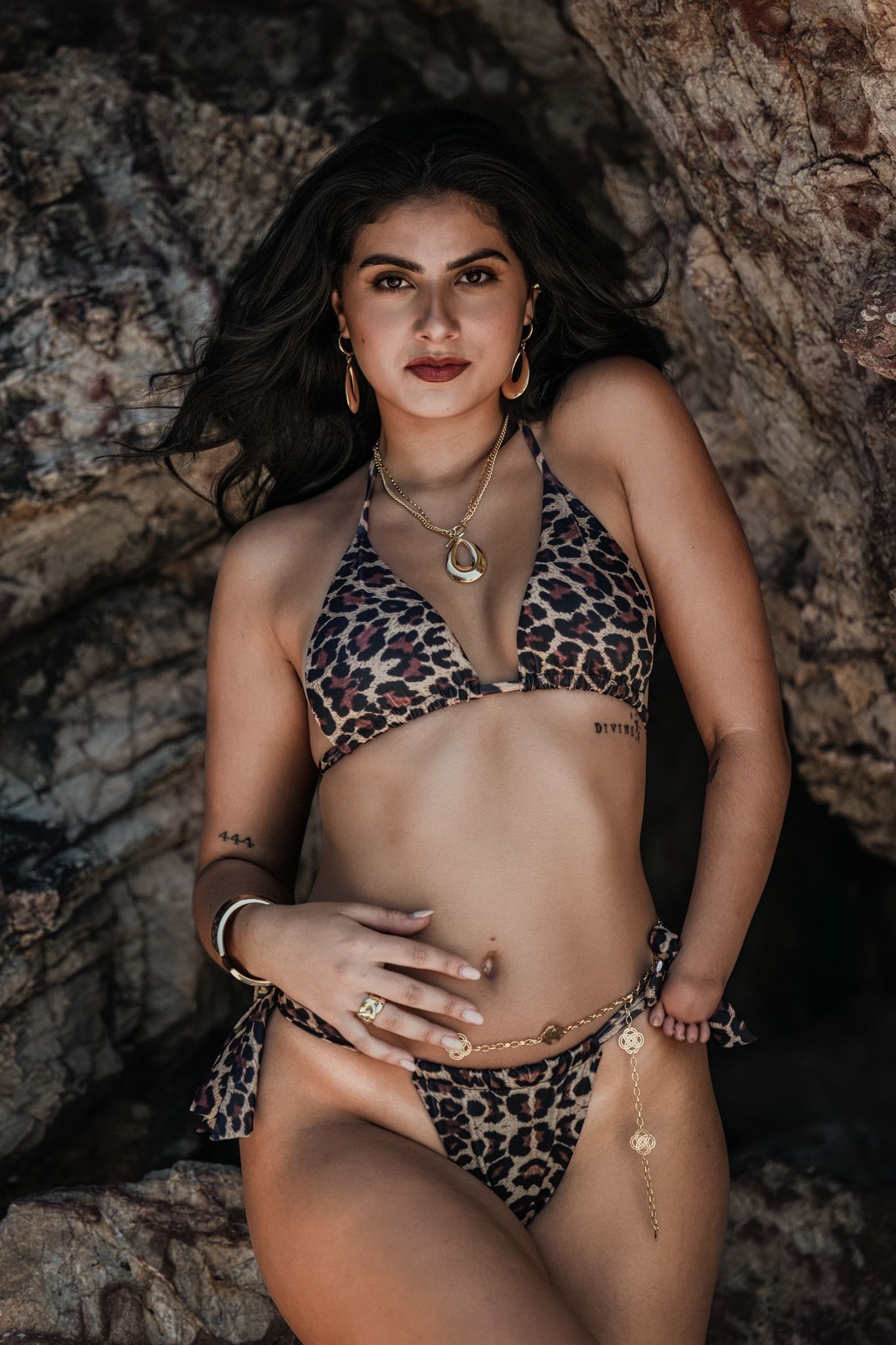 Fashion model in leopard print swimwear poses against textured rock wall background.