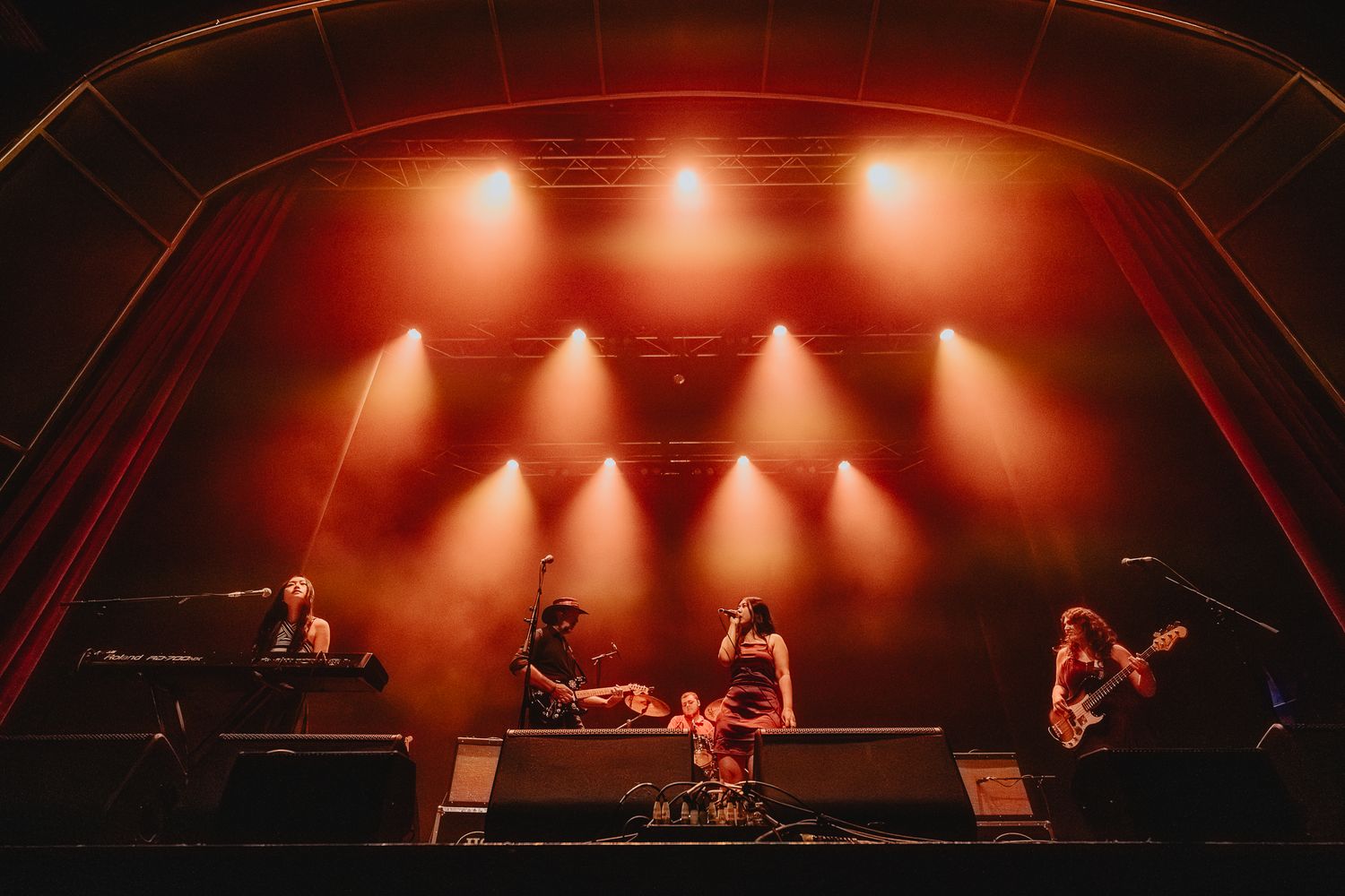 Wide concert stage view with warm orange lighting and silhouetted performers.