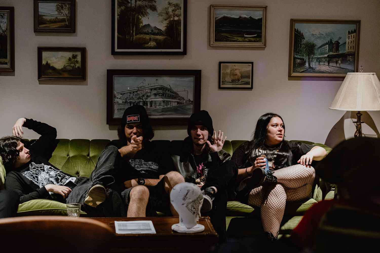 Band members relaxing on a vintage green couch surrounded by framed artwork.