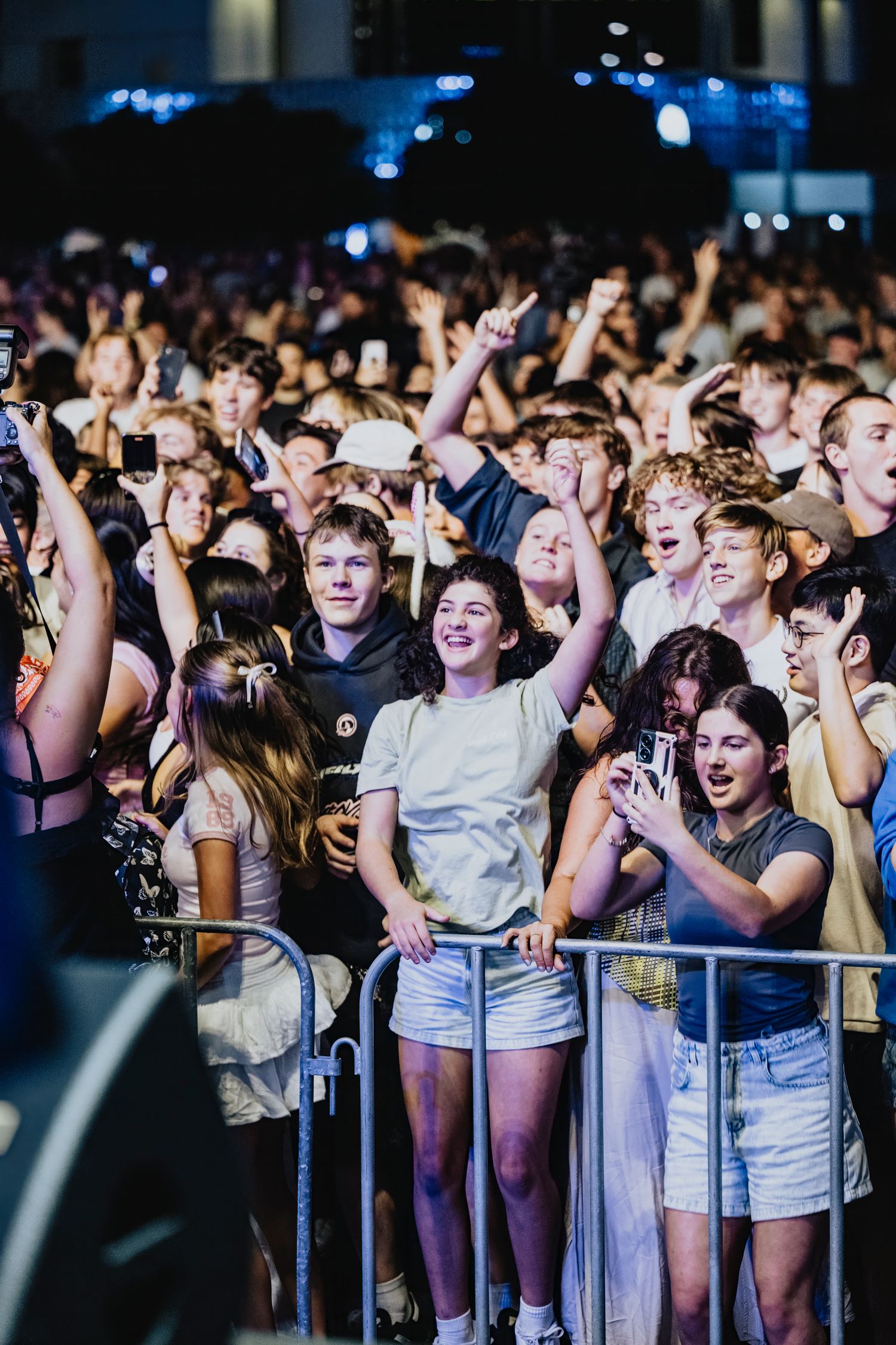 Excited concert crowd cheering and raising hands at a live music performance with blue stage lighting in the background.
