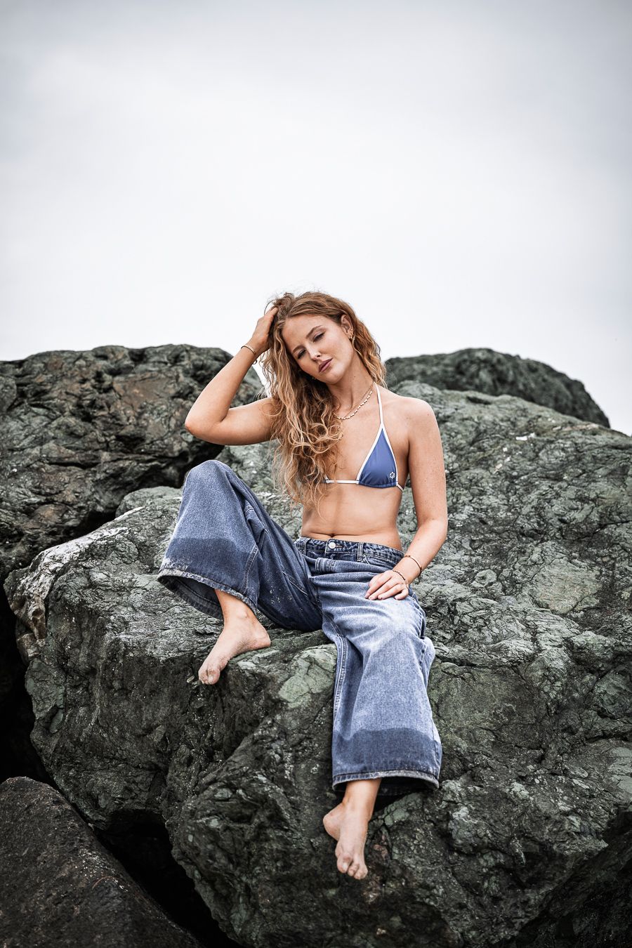 Figure reclining on dark rocky outcrop wearing casual denim and blue swimwear.