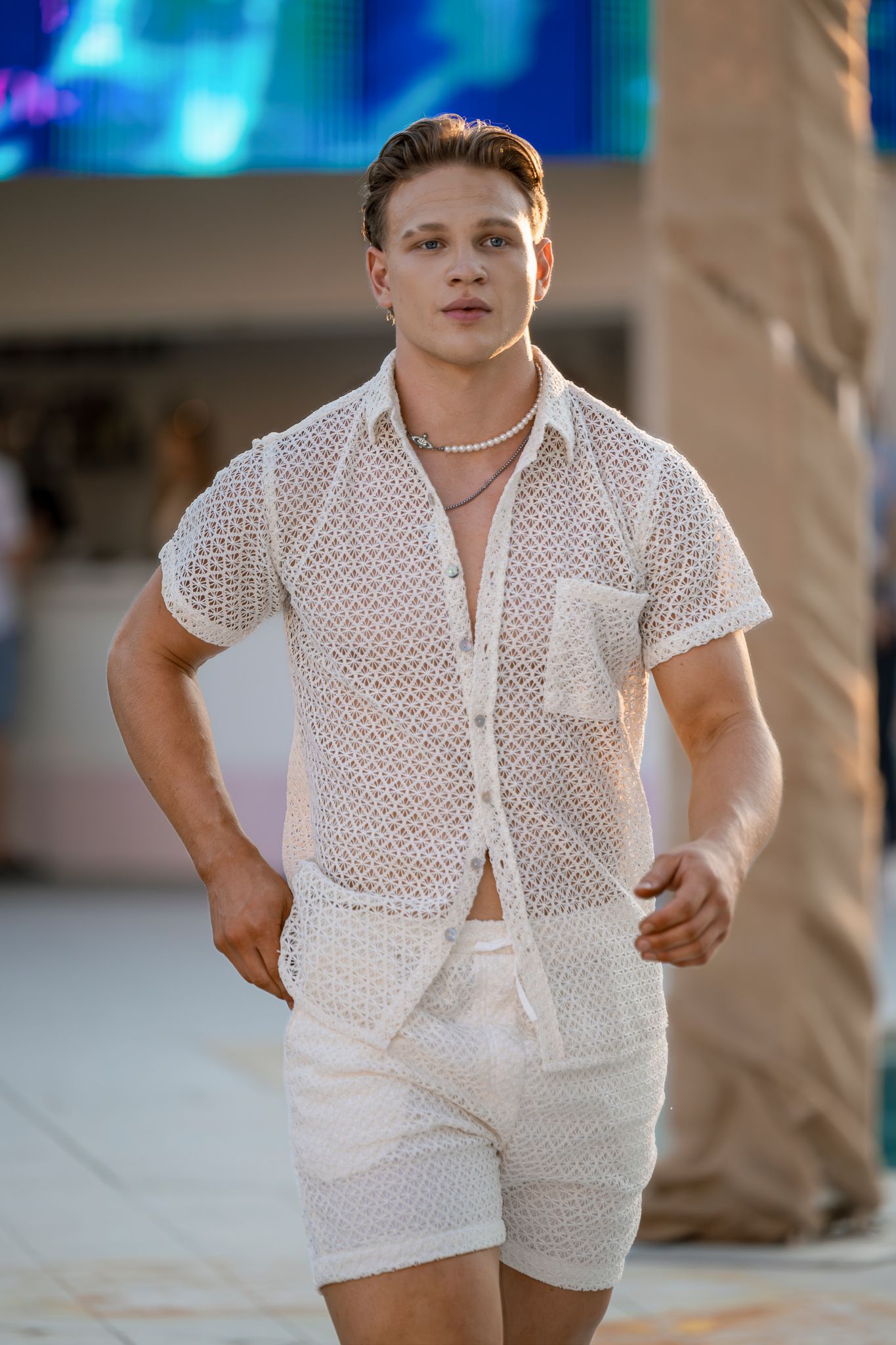 Model wearing all-white mesh button-down shirt and shorts at summer fashion show.