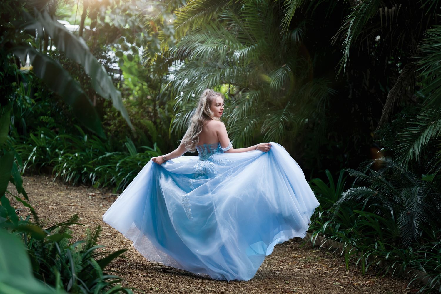 Flowing light blue dress captured in motion along garden path surrounded by tropical foliage.