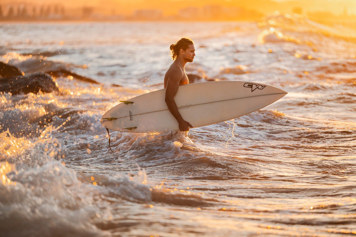 Surfer silhouettes in golden sunset water with surfboards.