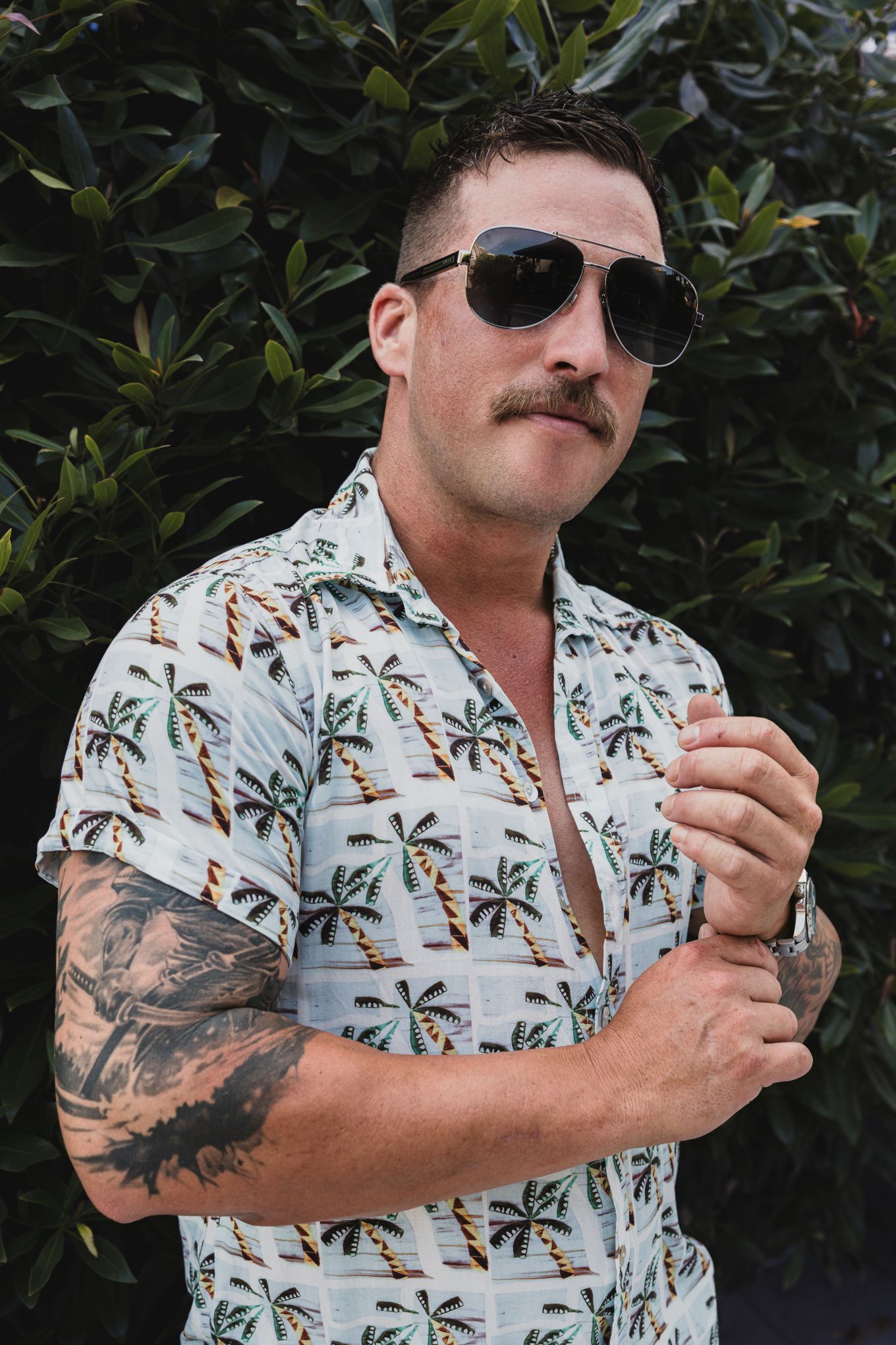 Person in tropical print shirt with sunglasses and mustache poses outdoors.