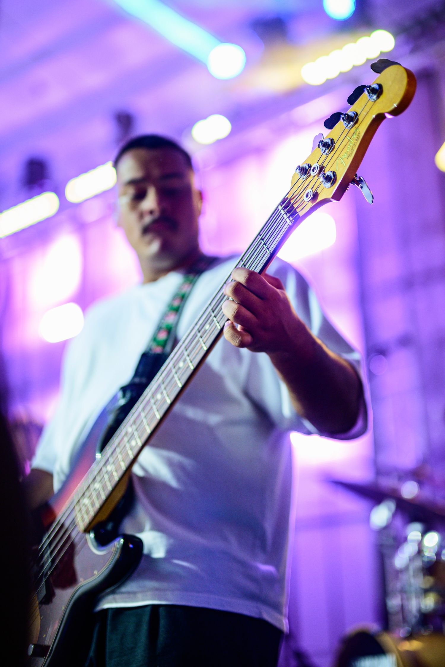Bass guitarist performing on stage with purple lighting effects.