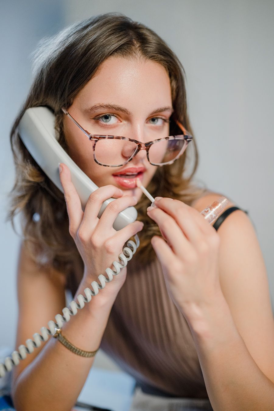 Person wearing glasses talking on a vintage corded telephone with animated expressions.