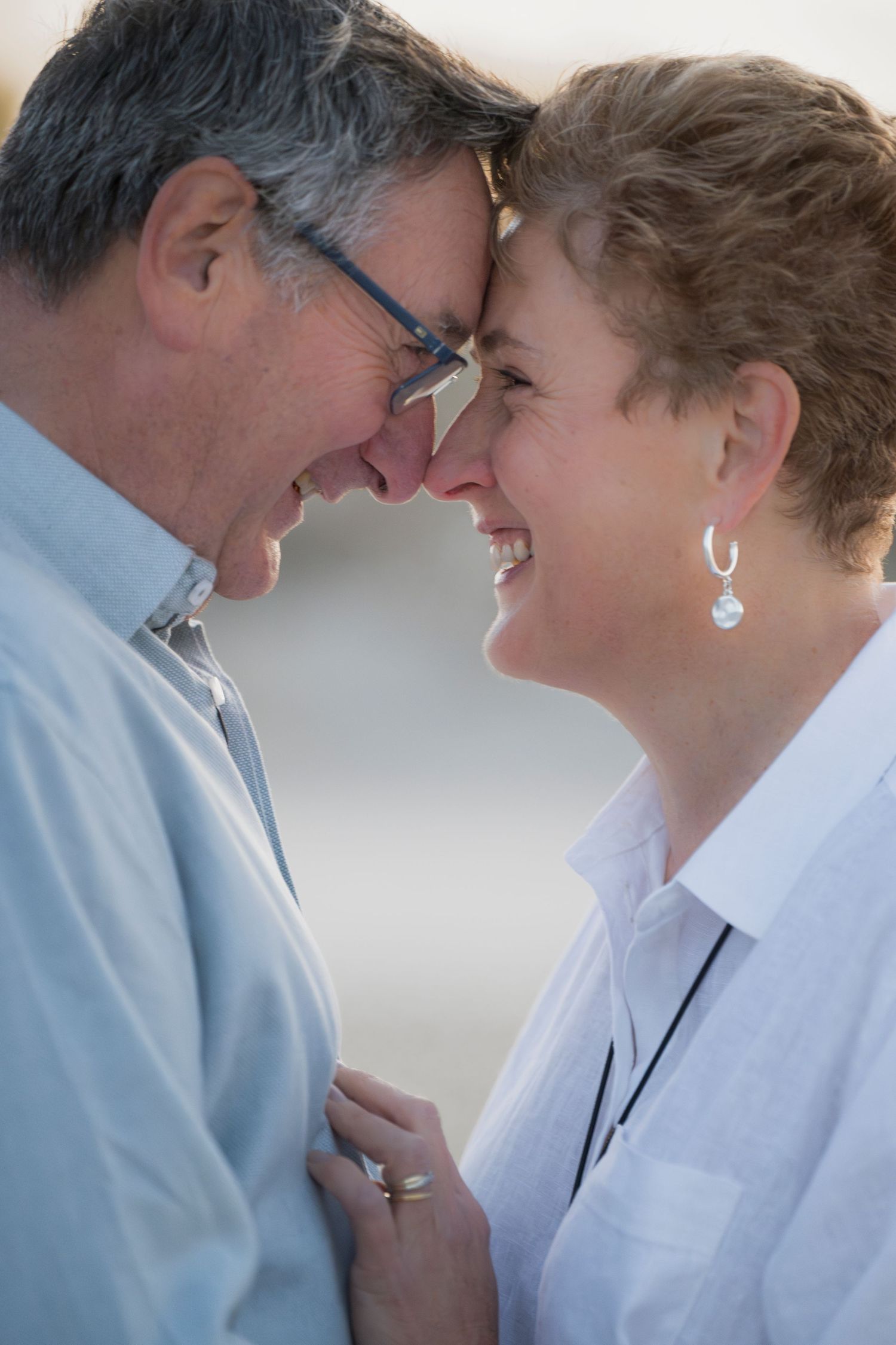 Smiling middle-aged couple touching foreheads affectionately, sharing a romantic moment outdoors.