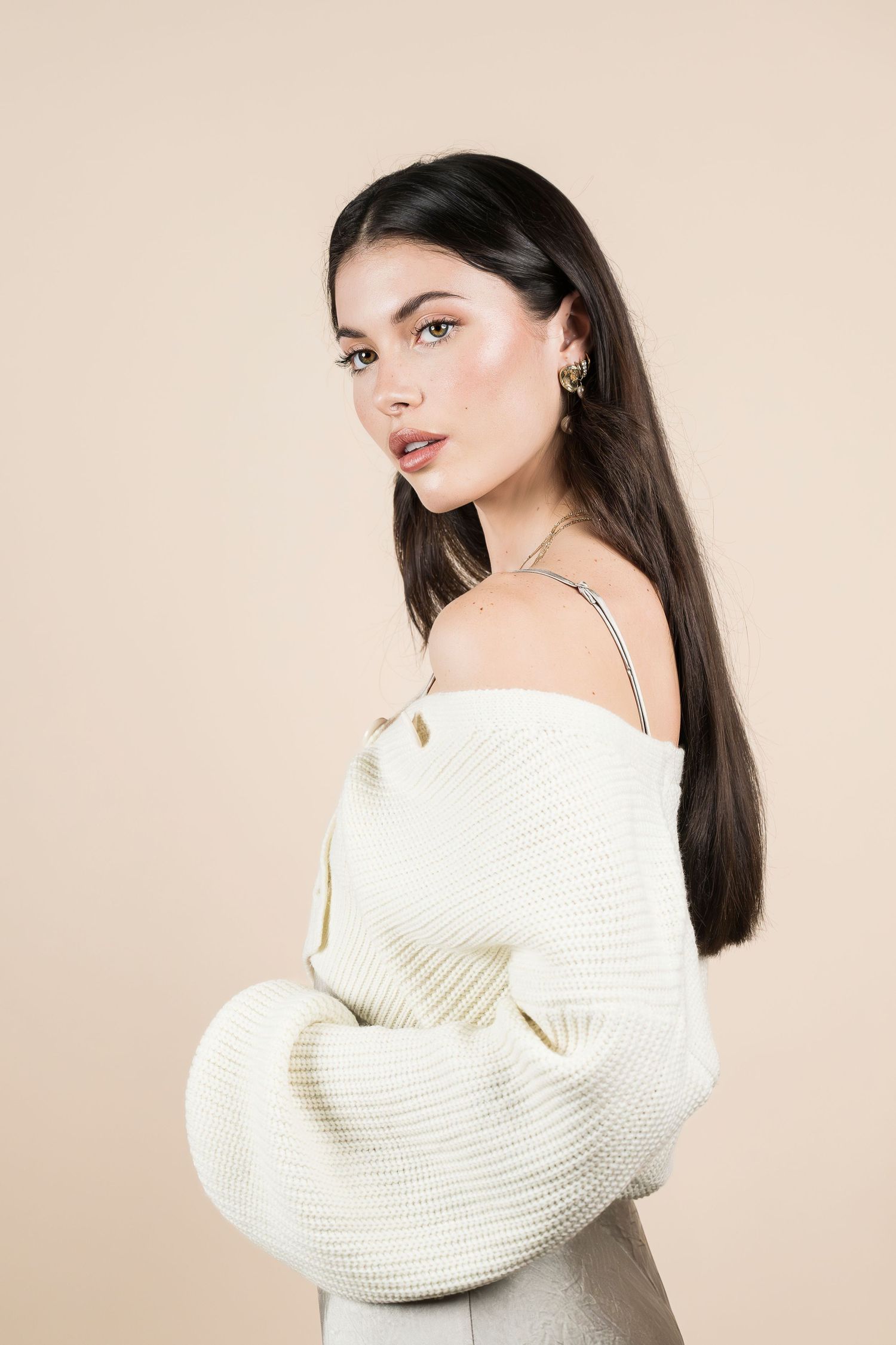 Fashion portrait of a person in white sweater against beige background.