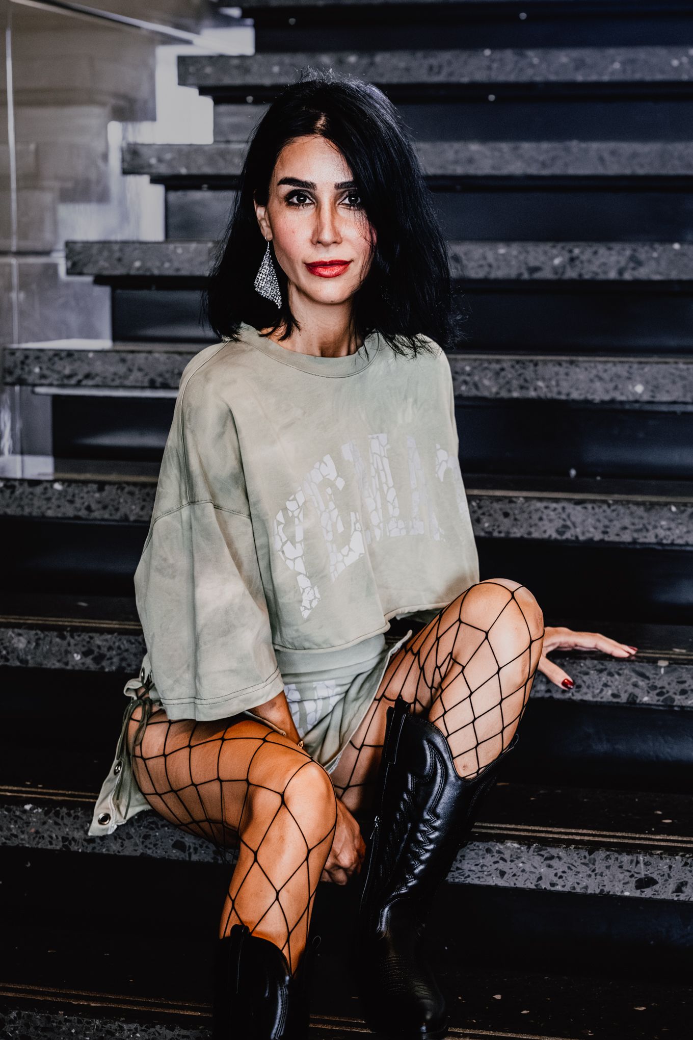 Edgy fashion portrait on concrete steps featuring fishnet tights and oversized sweater.