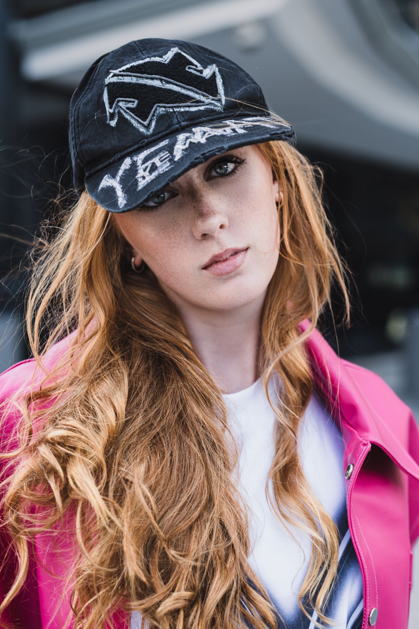 Close-up fashion portrait wearing black baseball cap and bright pink jacket.