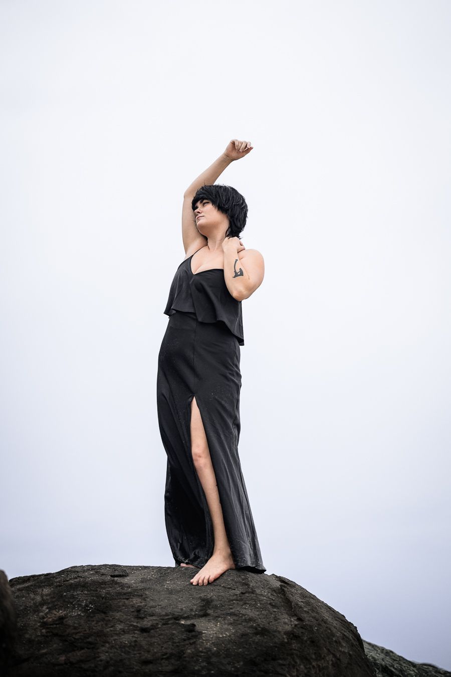 Artistic silhouette of person in black dress standing on rocky formation.