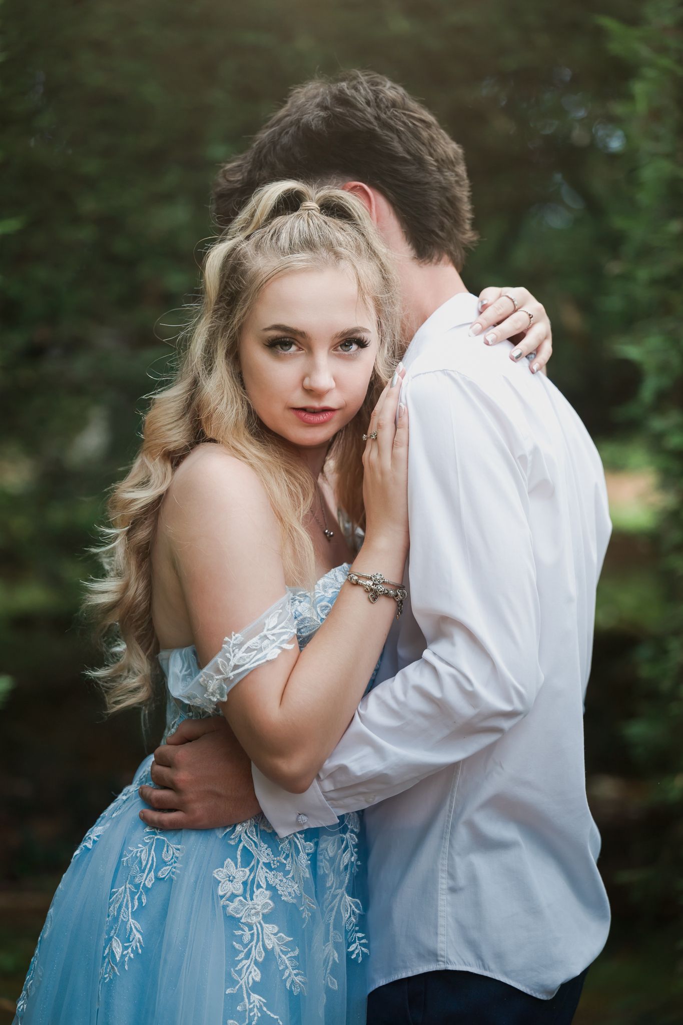 Romantic couple in a garden setting with woman wearing blue embellished dress and man in white shirt.