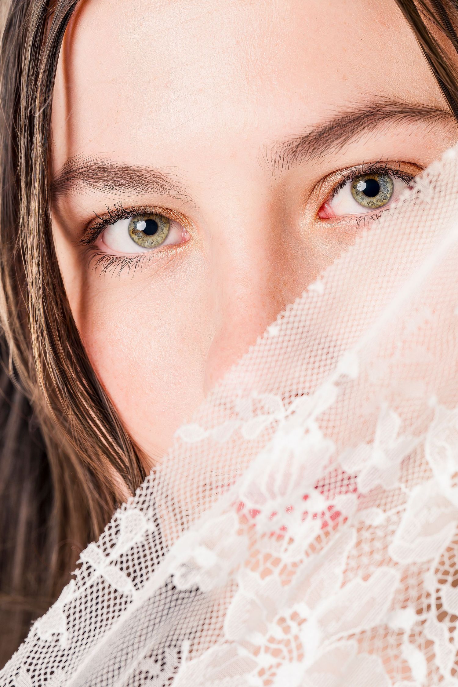 Close-up portrait partially covered by white lace veil.