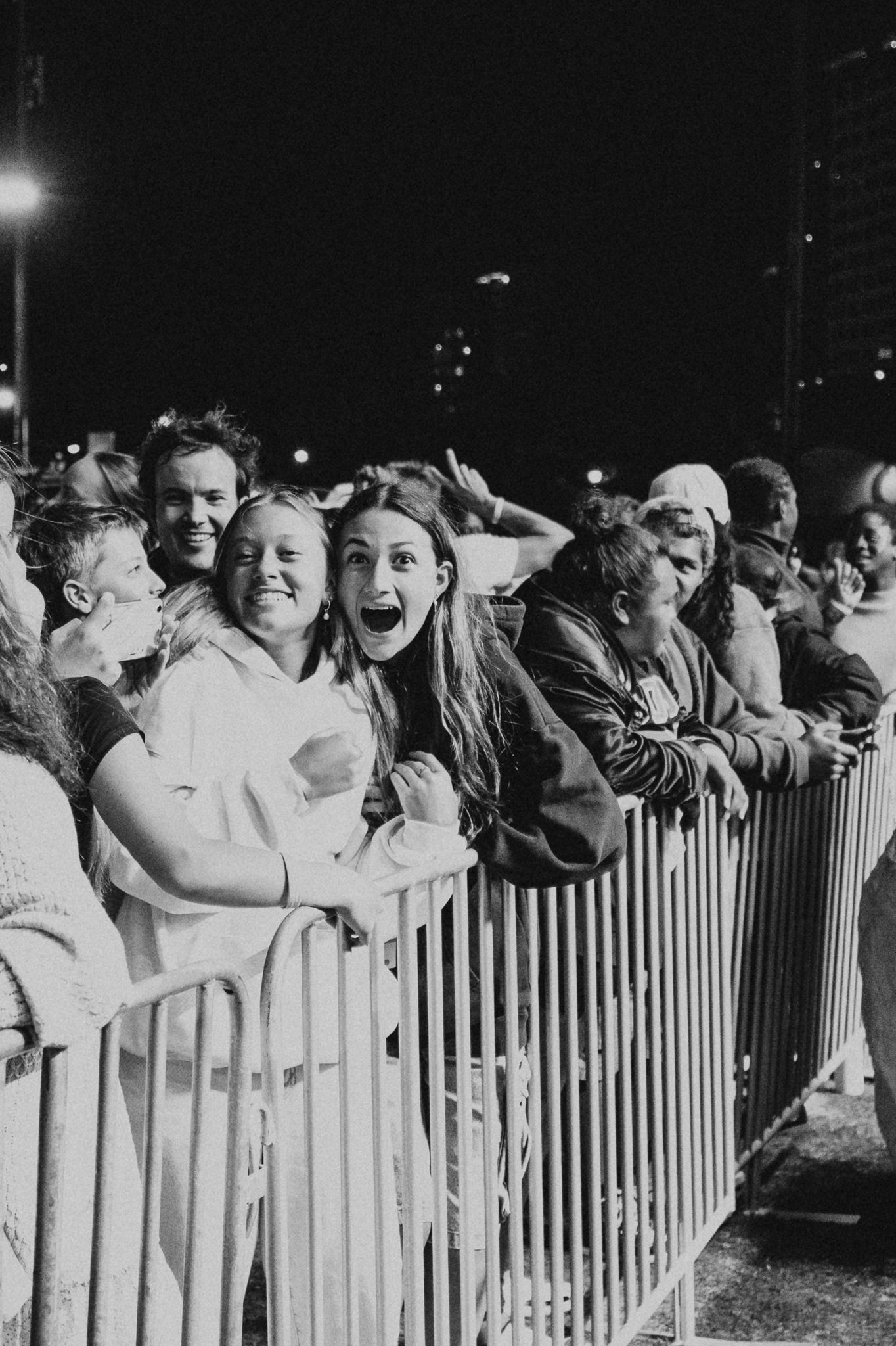 Excited crowd of fans behind metal barriers at a nighttime outdoor event.
