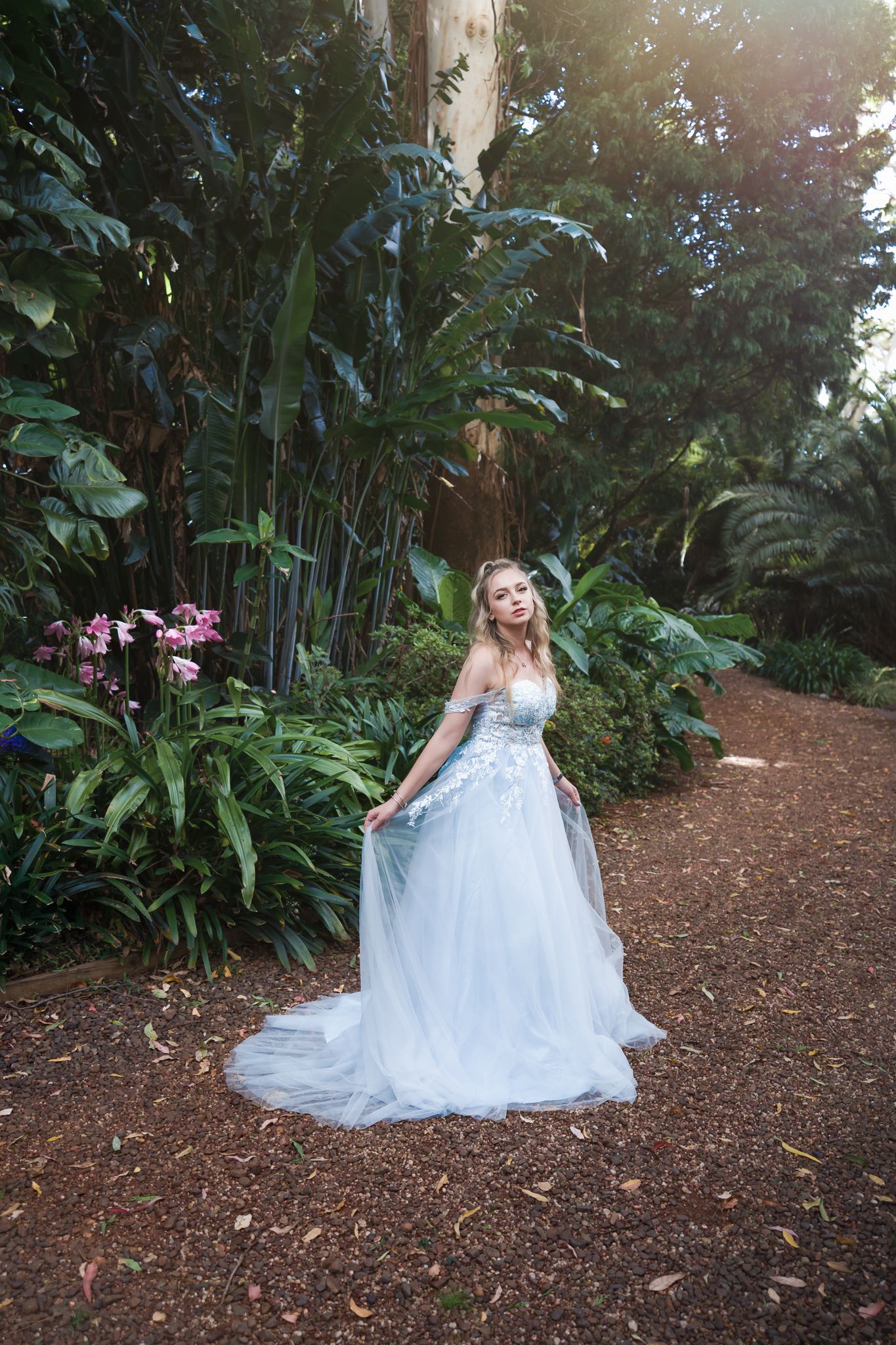 Light blue ballgown dress photographed in lush garden setting with dappled sunlight.