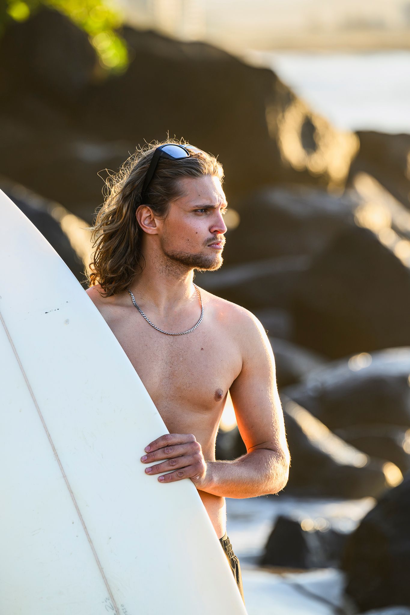 Surfer holding white surfboard against rocky coastline.