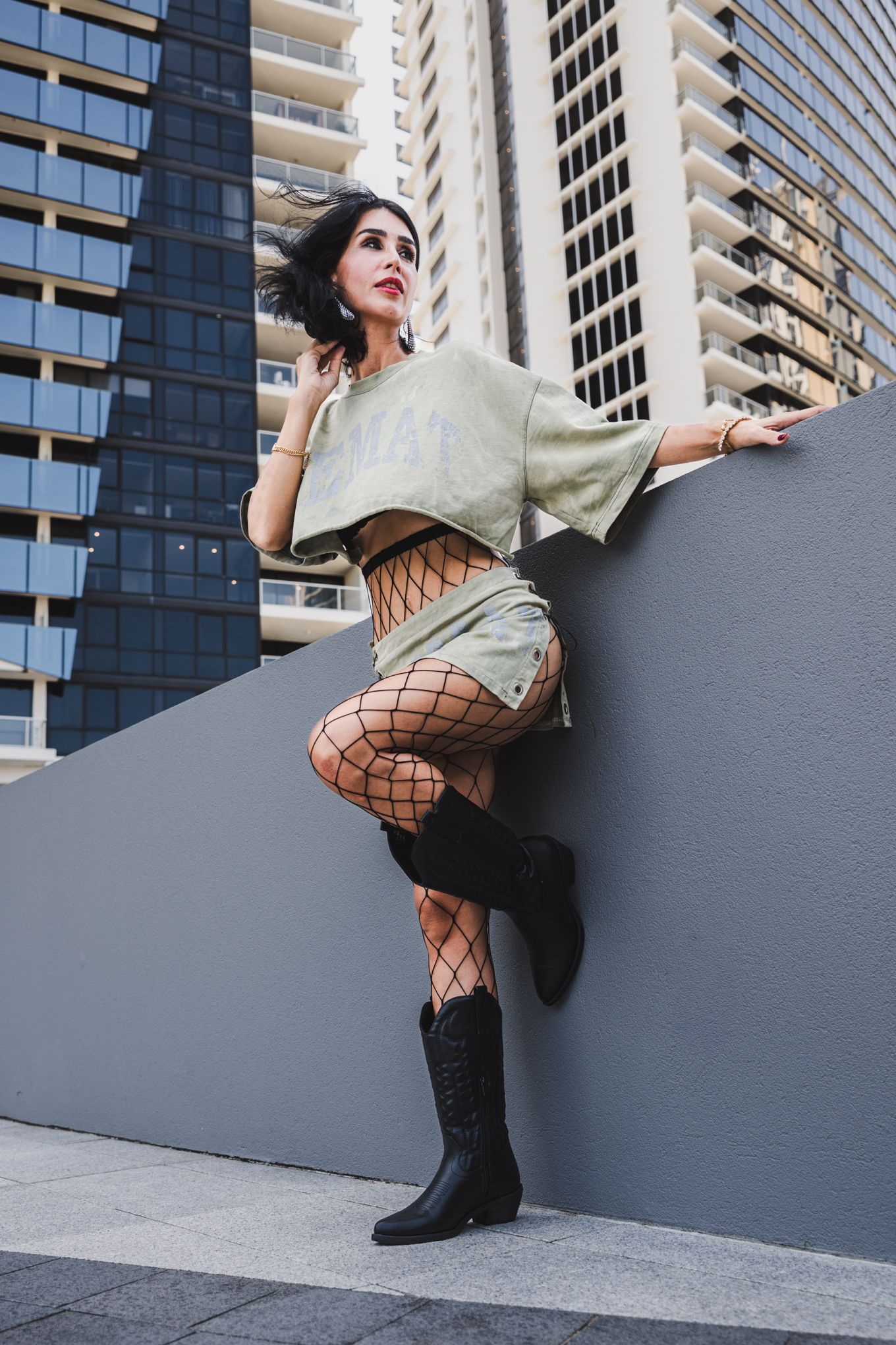 Urban fashion shot featuring edgy outfit with fishnet stockings and boots against city backdrop.