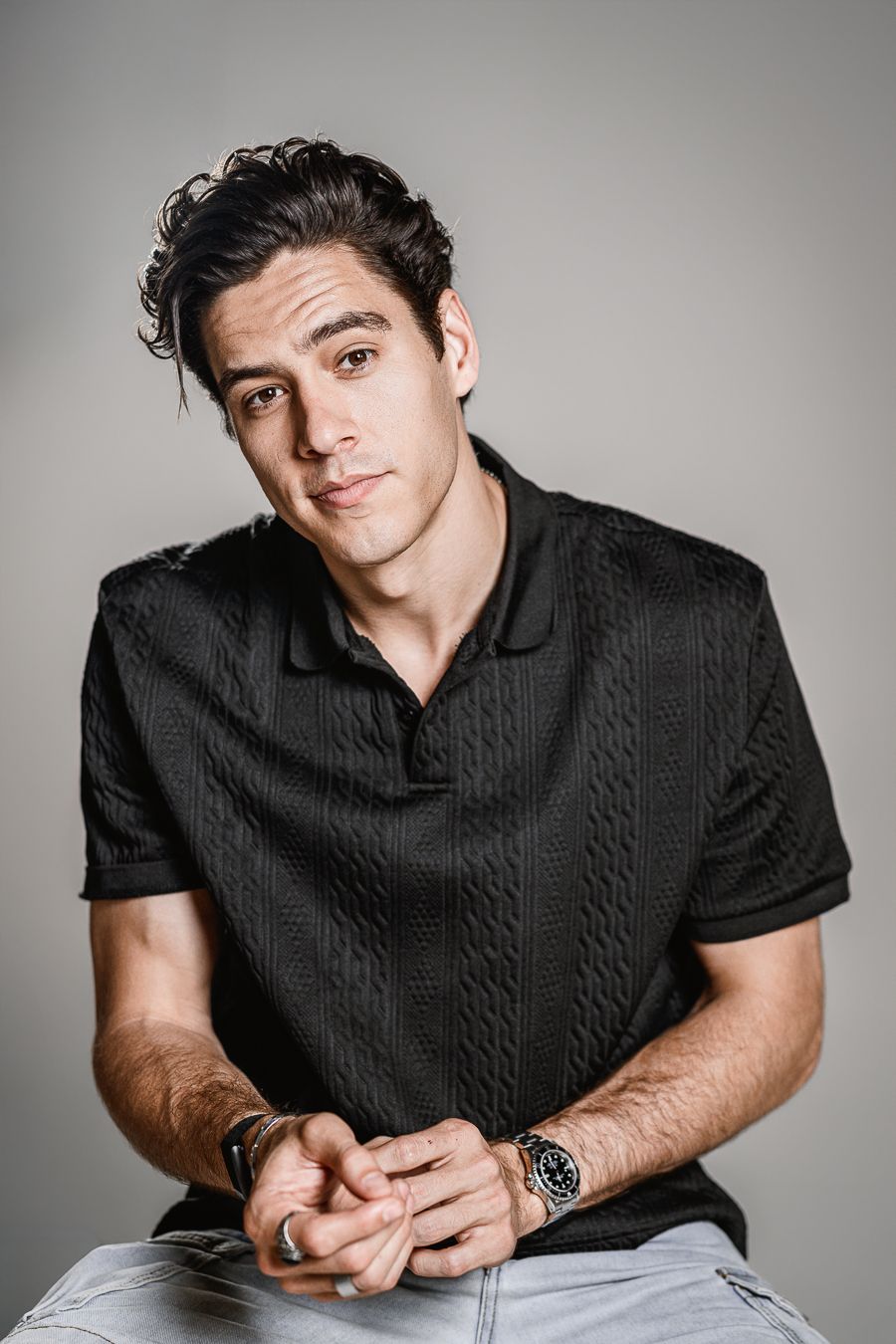 Studio portraits featuring a person wearing a black cable knit polo shirt against a gray background.